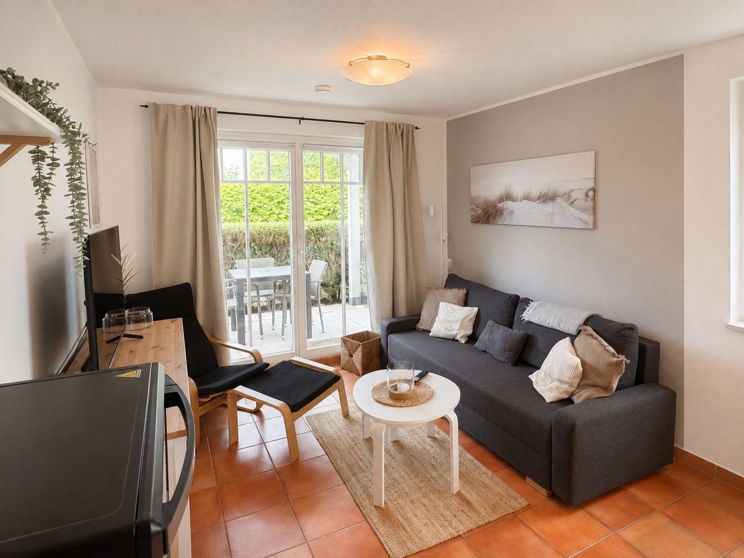 Wohnzimmer mit Sofa, Couchtisch und Blick auf Balkon mit Tisch und Stühlen.