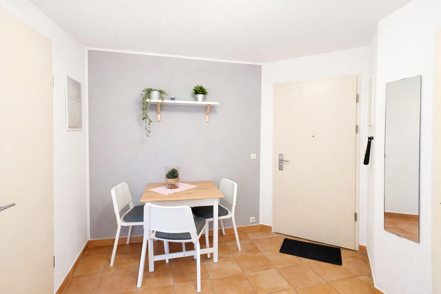 Esszimmer mit Tisch, vier Stühlen und Wandregal mit Pflanzen.