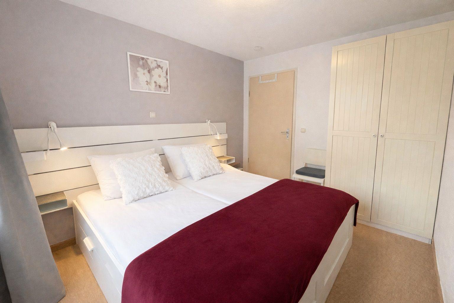 Schlafzimmer mit Doppelbett, Kleiderschrank und Wandbild.