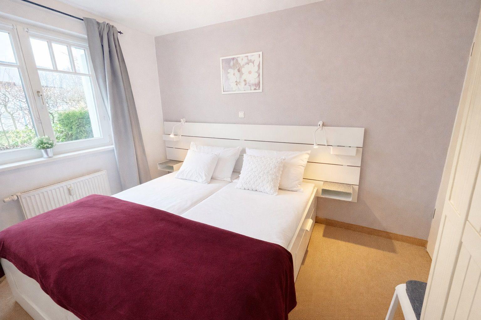 Schlafzimmer mit Doppelbett, Fenster und Wandbild.