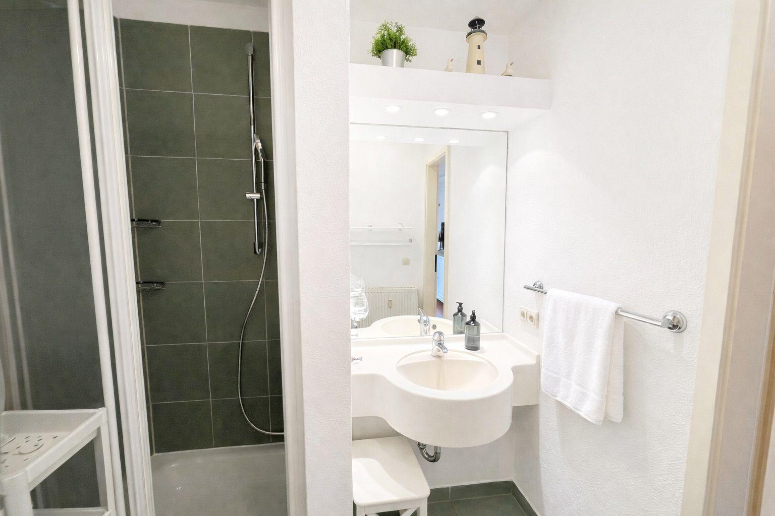 Bad mit Dusche, Waschbecken und Spiegel. Handtuch und Dekoration sind vorhanden.