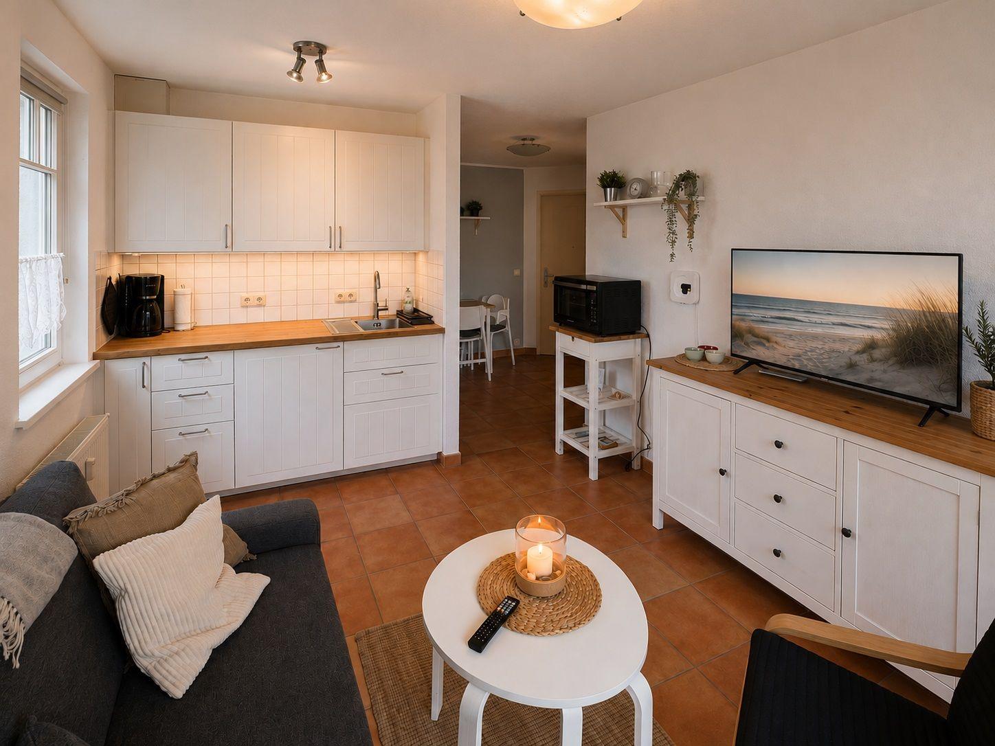 Wohnküche mit Sofa, TV und Küchenschränken. Terrakottafußboden und Holzoberflächen.