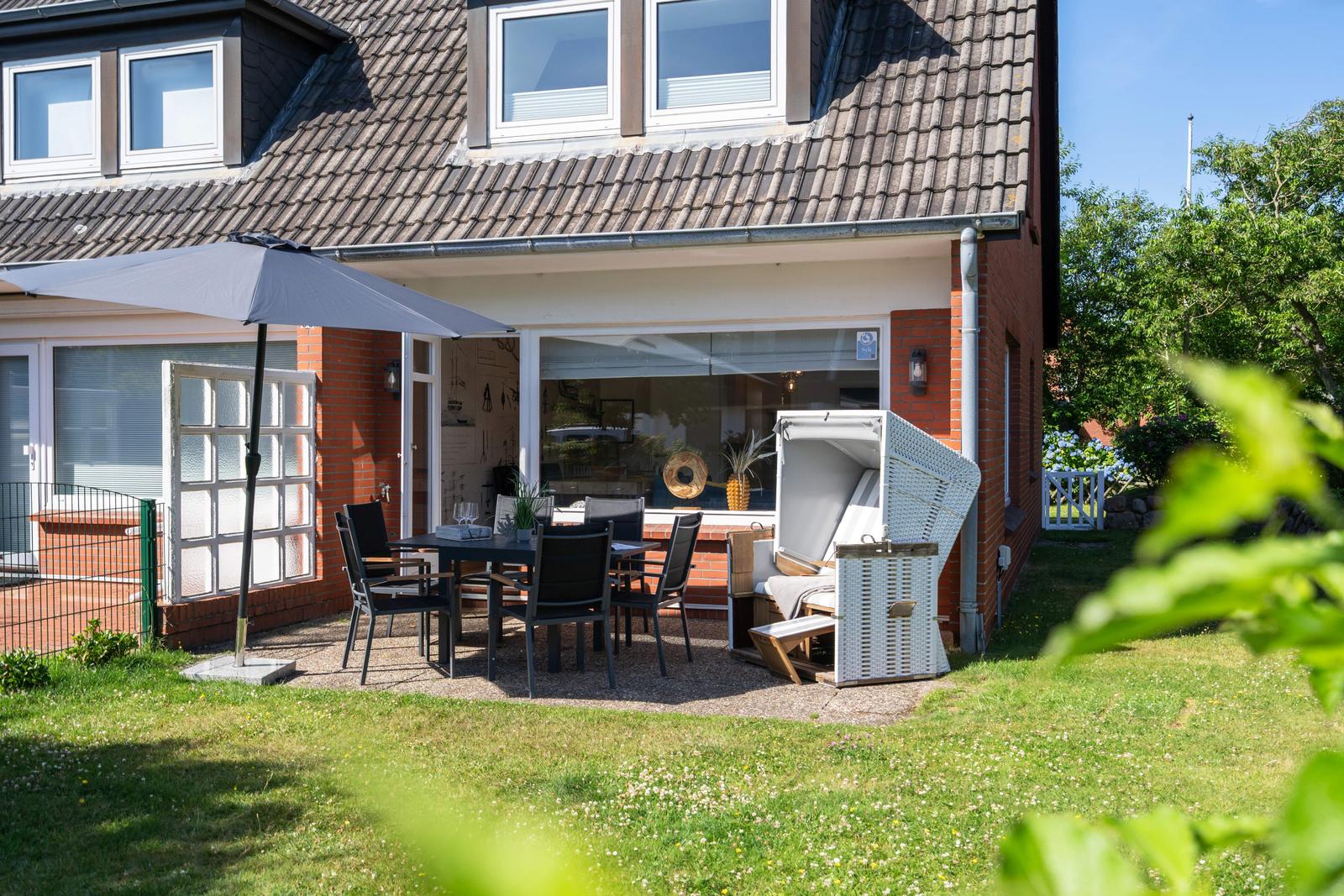 Terrasse mit Tisch, Stühlen und Sonnenschirm neben einem Haus mit Garten.