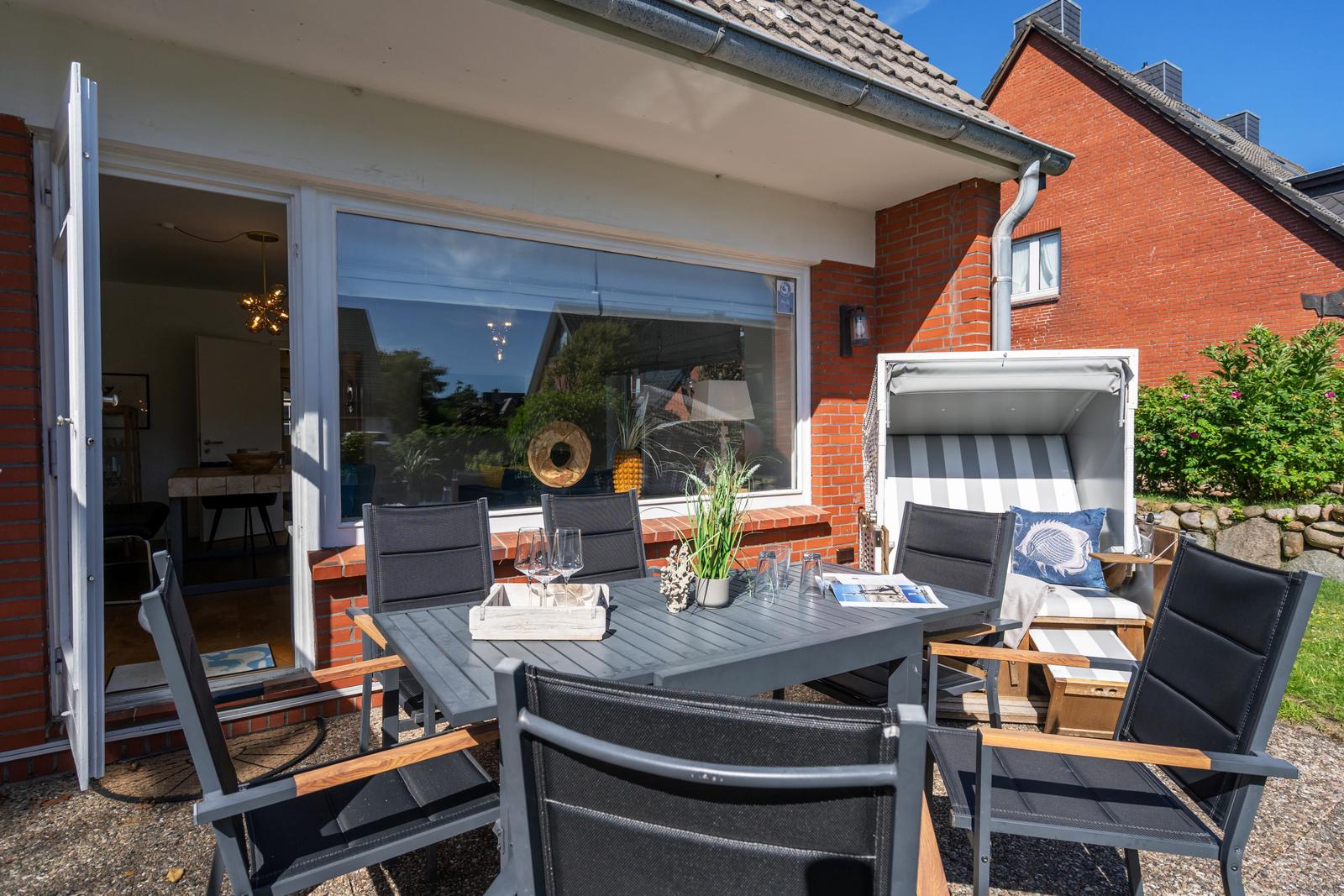 Terrasse mit Tisch, Stühlen und Liege. Durchgang ins Haus. Blick auf Garten und Nachbarhaus.