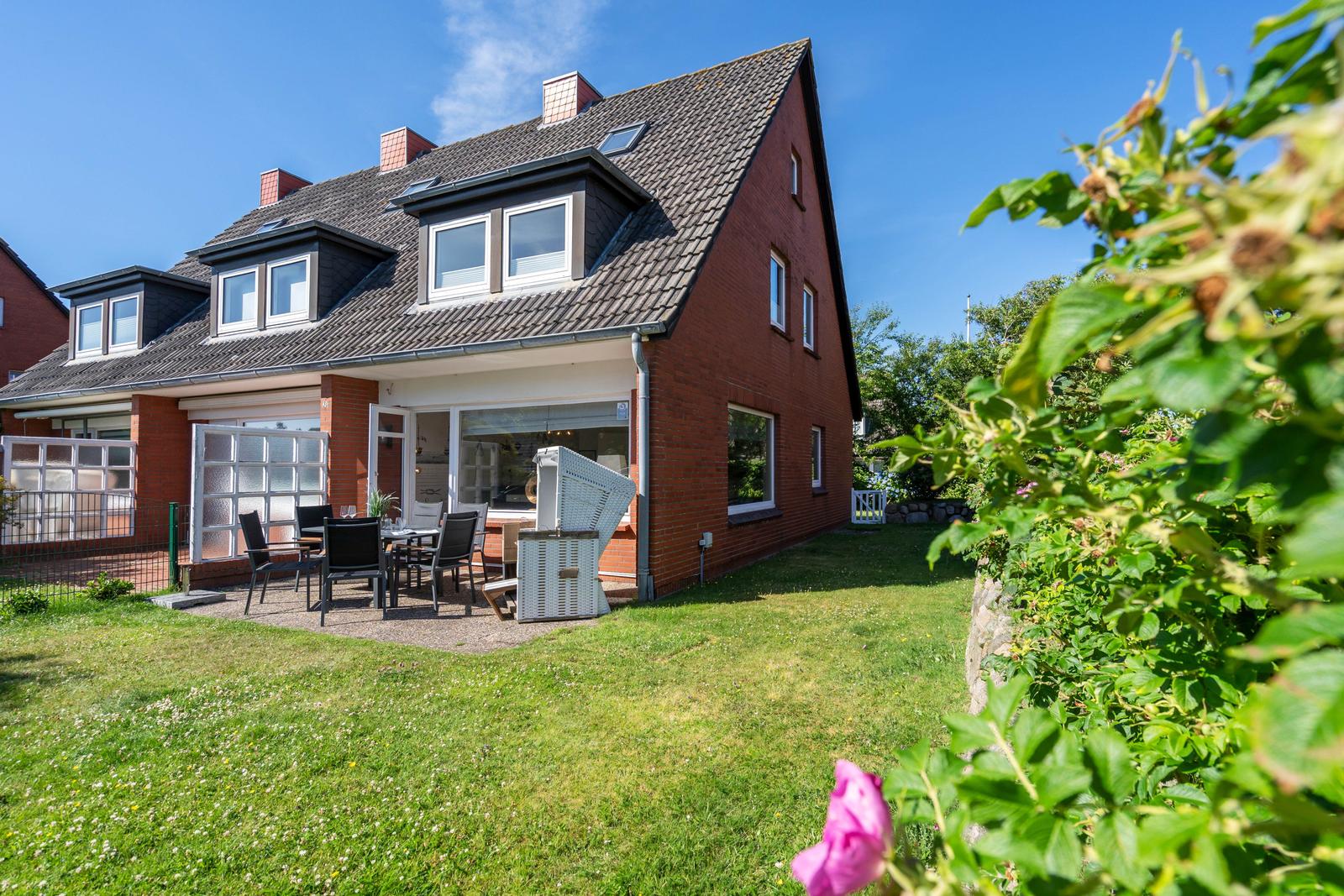 Rotes Haus mit Terrasse und Garten. Außentisch mit Stühlen und Sicht auf Wohnbereich.