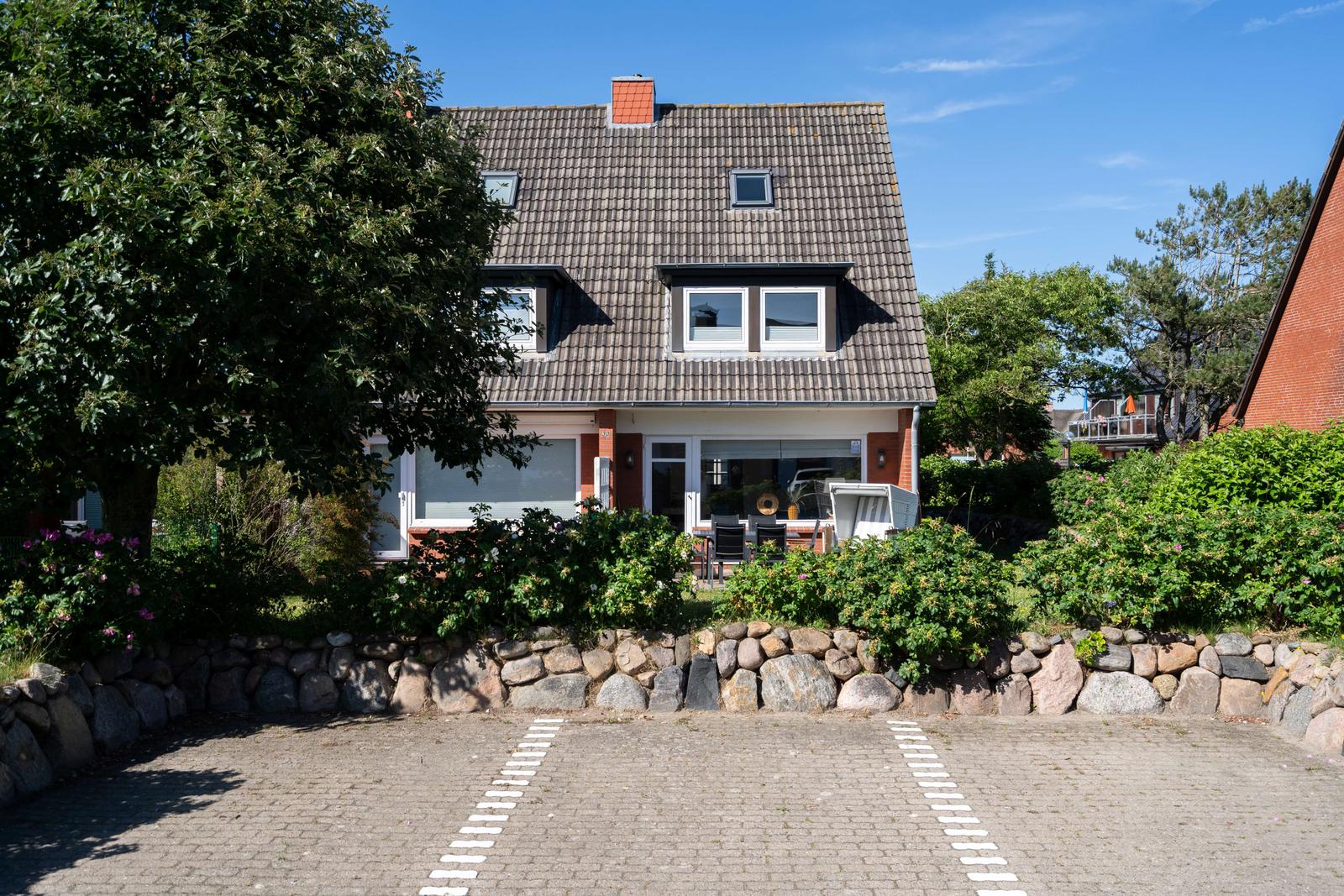 Ein Haus mit Dachfenstern und Garten, umgeben von Bäumen und einem Steinzaun.
