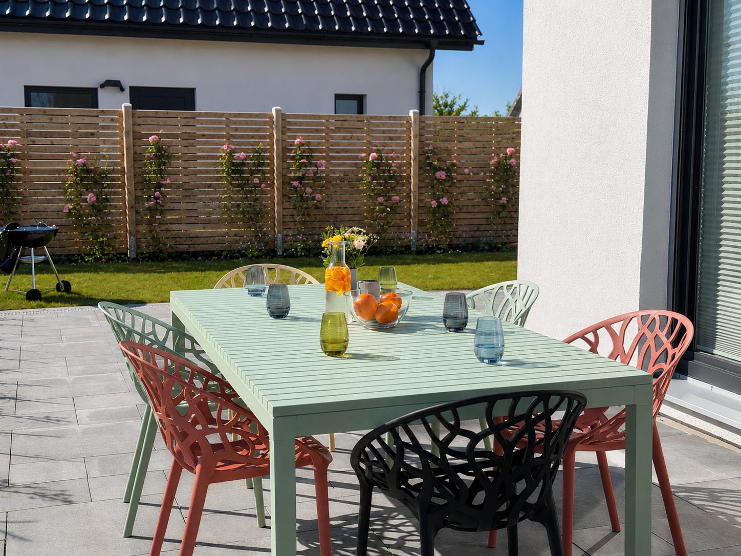 Terrasse mit Tisch und Stühlen, Grill und Beet mit Rosen.