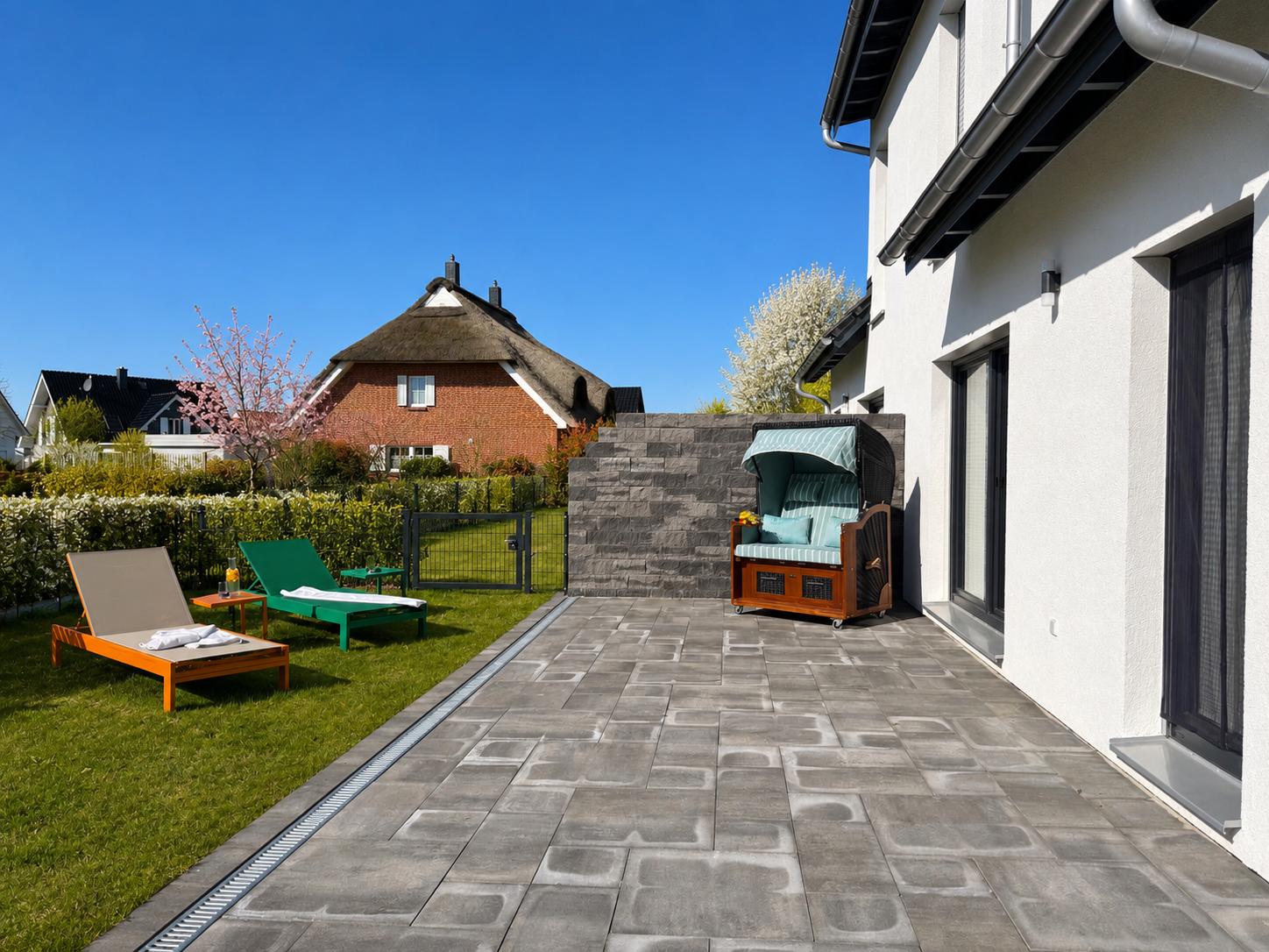 Terrasse mit Liegestühlen und Garten. Hinterhof mit Steinmauer und Grünflächen.