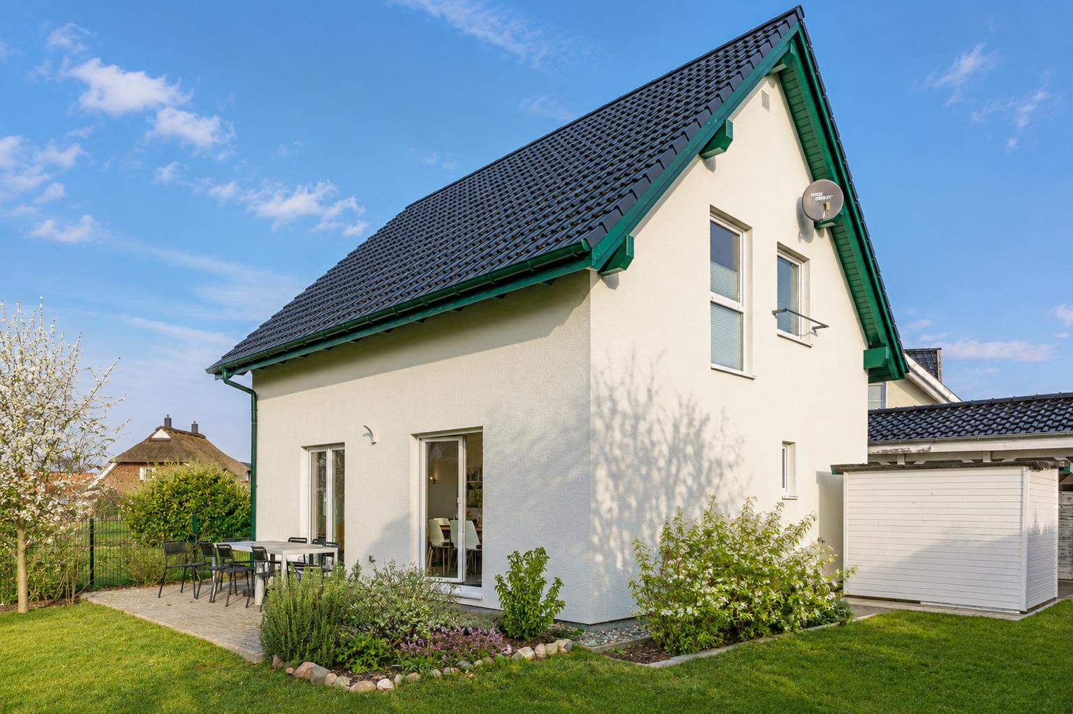 Ein Haus mit grünem Dachrand, Terrasse und Garten. Satellitenschüssel an der Wand.