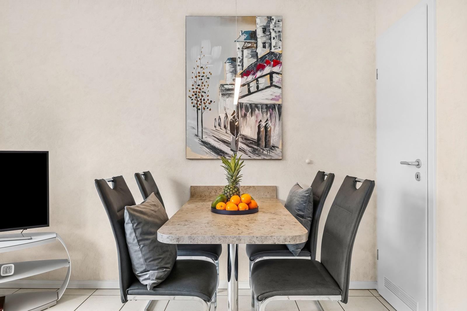 Esstisch mit sechs Stühlen, Obstschale und Wandbild.