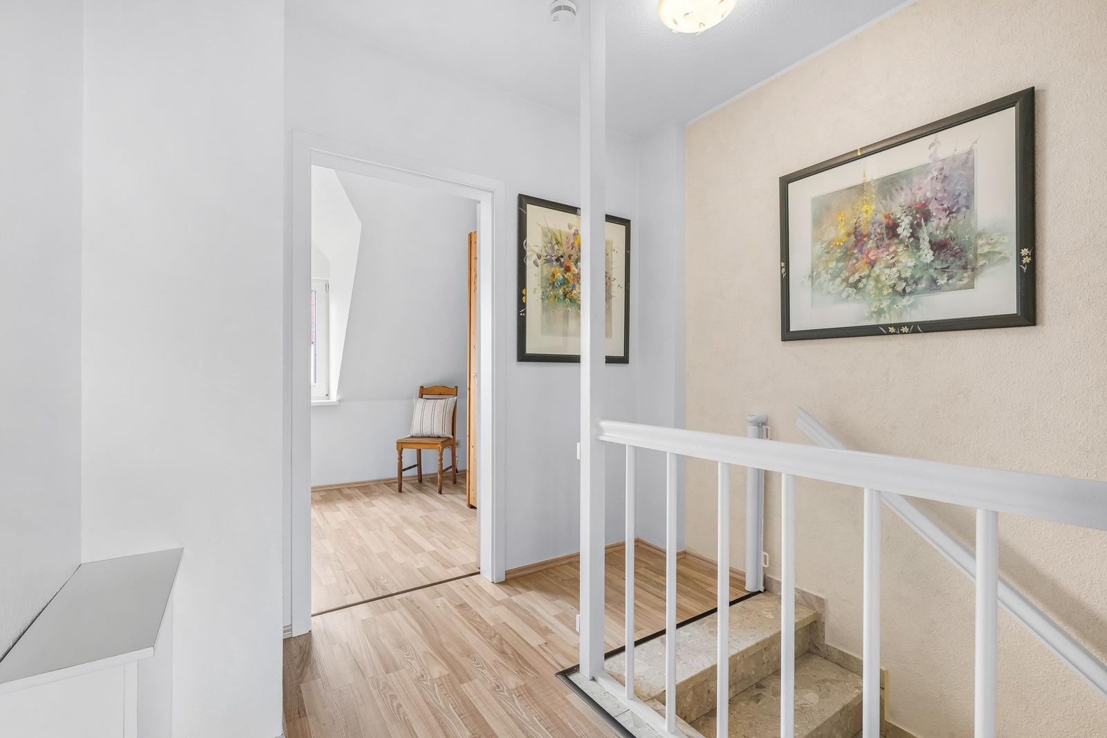 Hausflur mit Treppe, Bildern an der Wand und Holzboden im angrenzenden Raum.
