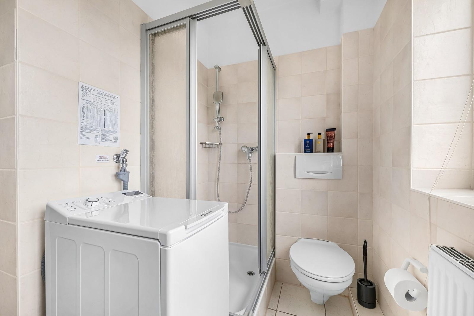 Badezimmer mit Dusche, Toilette und Waschmaschine.