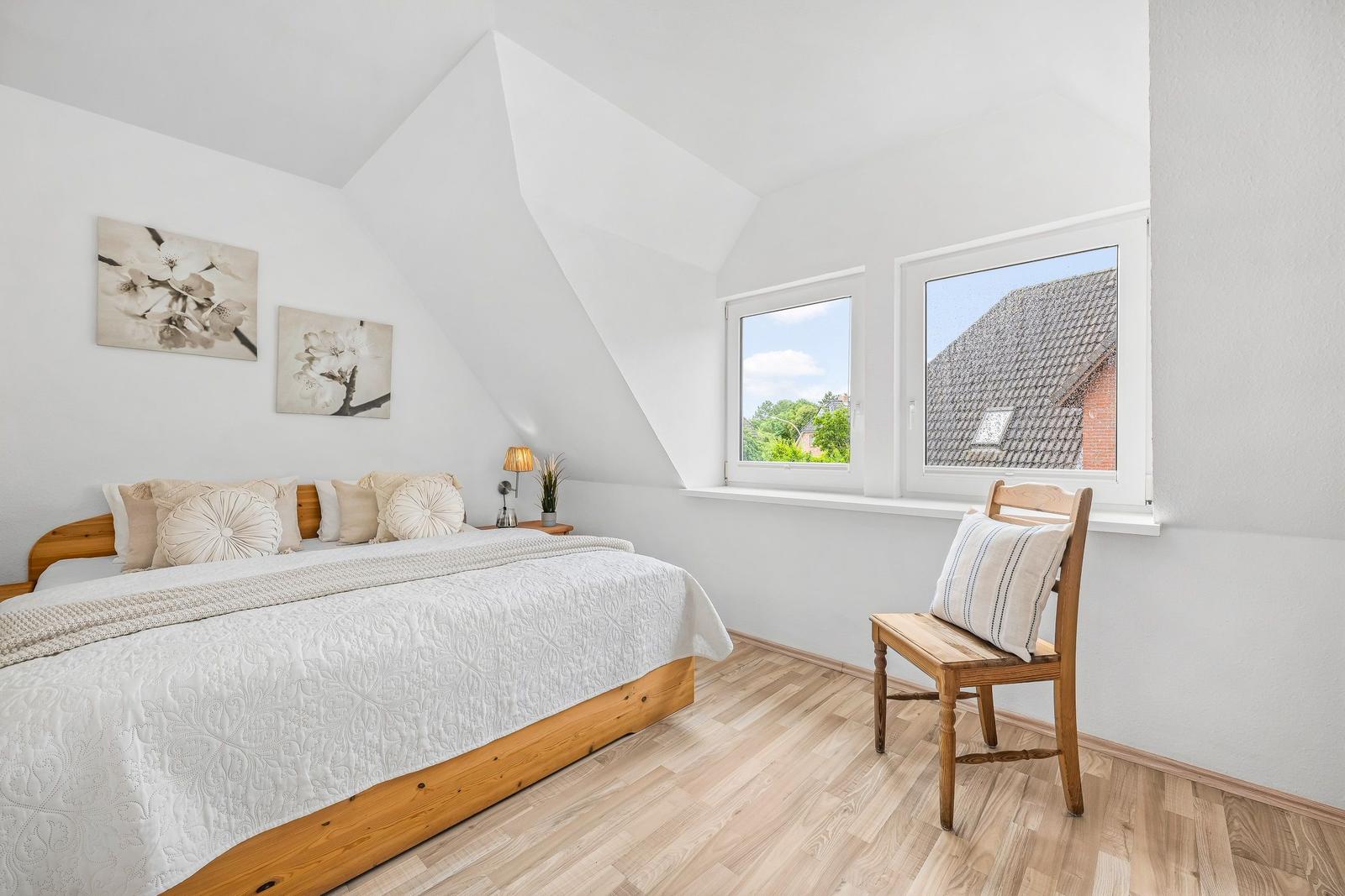 Schlafzimmer mit Dachschrägen, Bett, Stuhl und Fenster mit Blick auf Dach