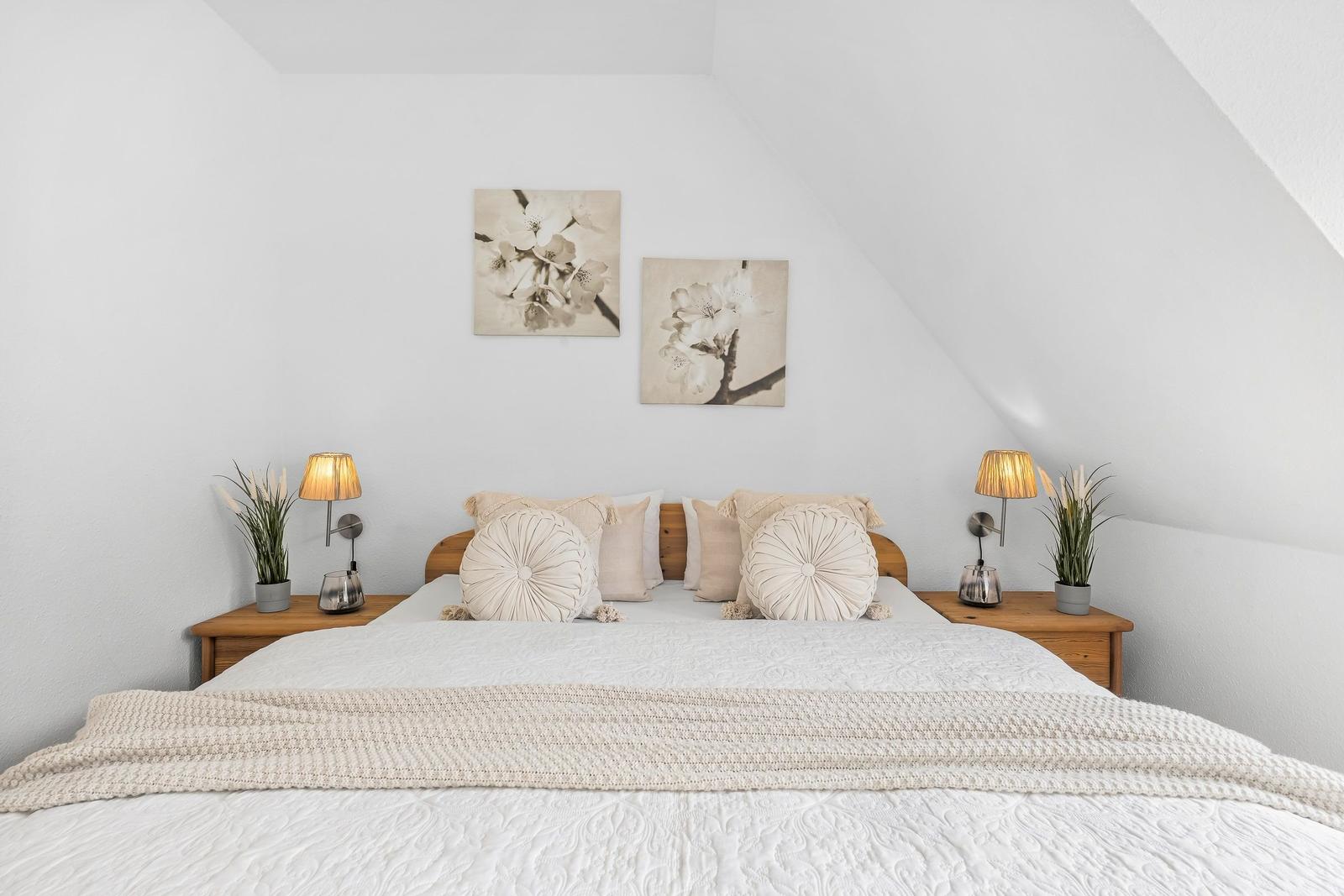 Schlafzimmer mit Dachschrägen, Bett mit Kissen, Nachttische und Wandbildern.