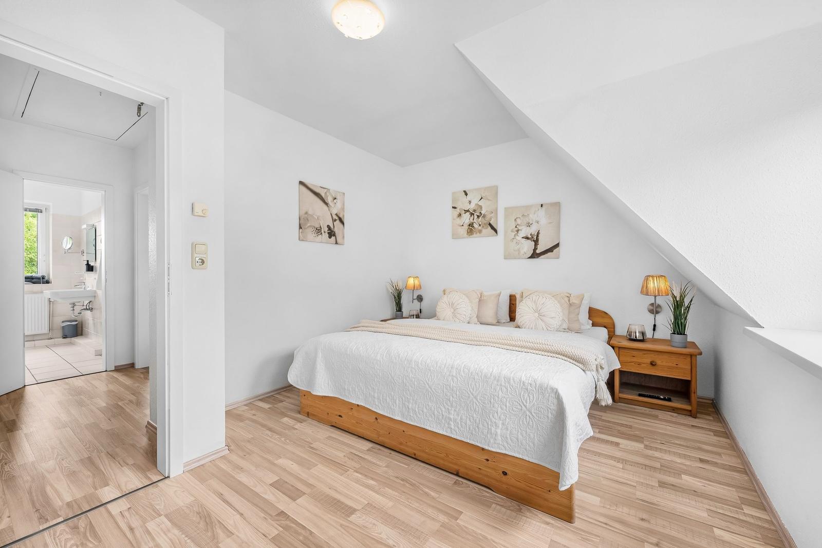 Schlafzimmer mit Holzboden, Dachschräge und Bett. Nebenraum ist Bad.