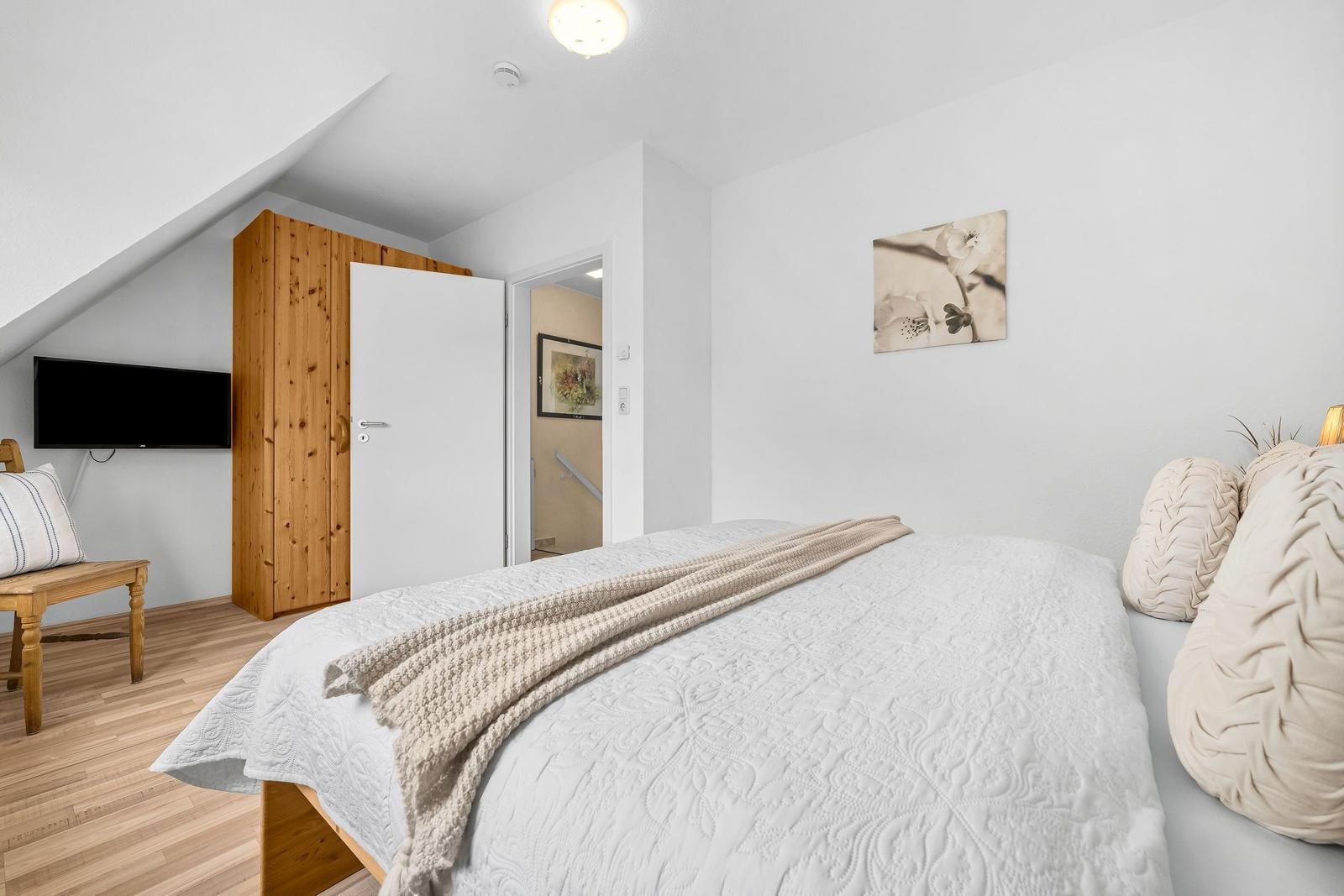 Schlafzimmer mit Bett, Kleiderschrank und Fernseher an der Wand.