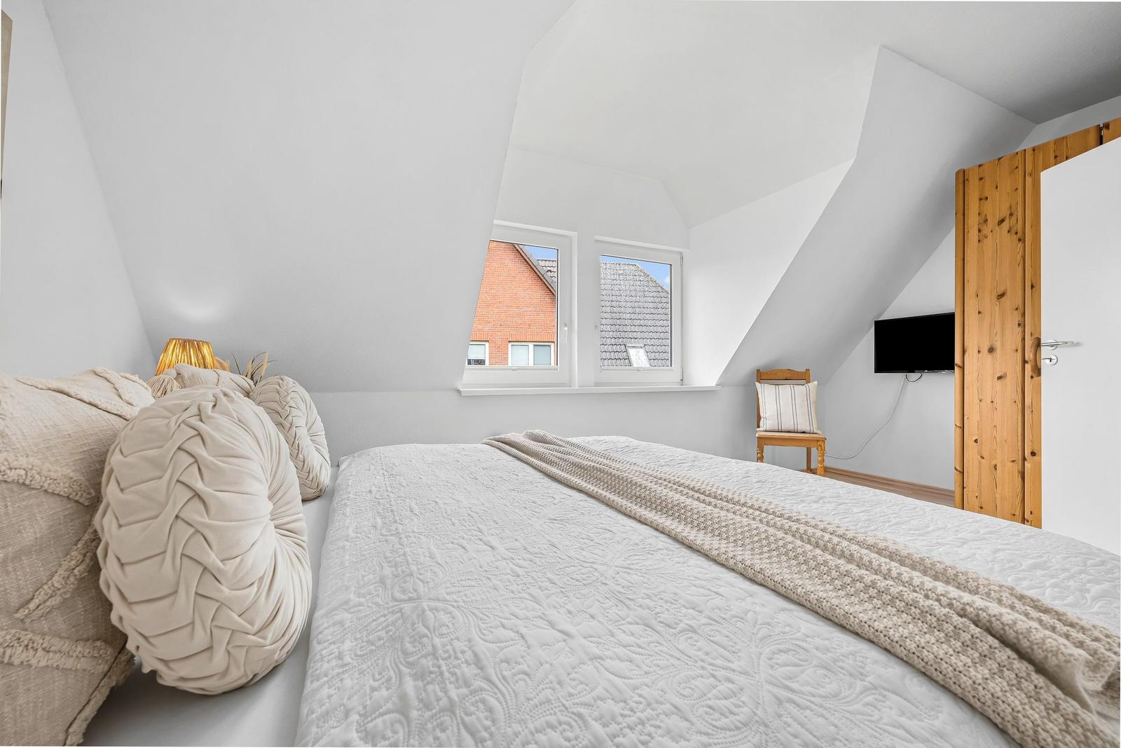 Schlafzimmer mit Dachschrägen, Bett, Fenster und Fernseher.