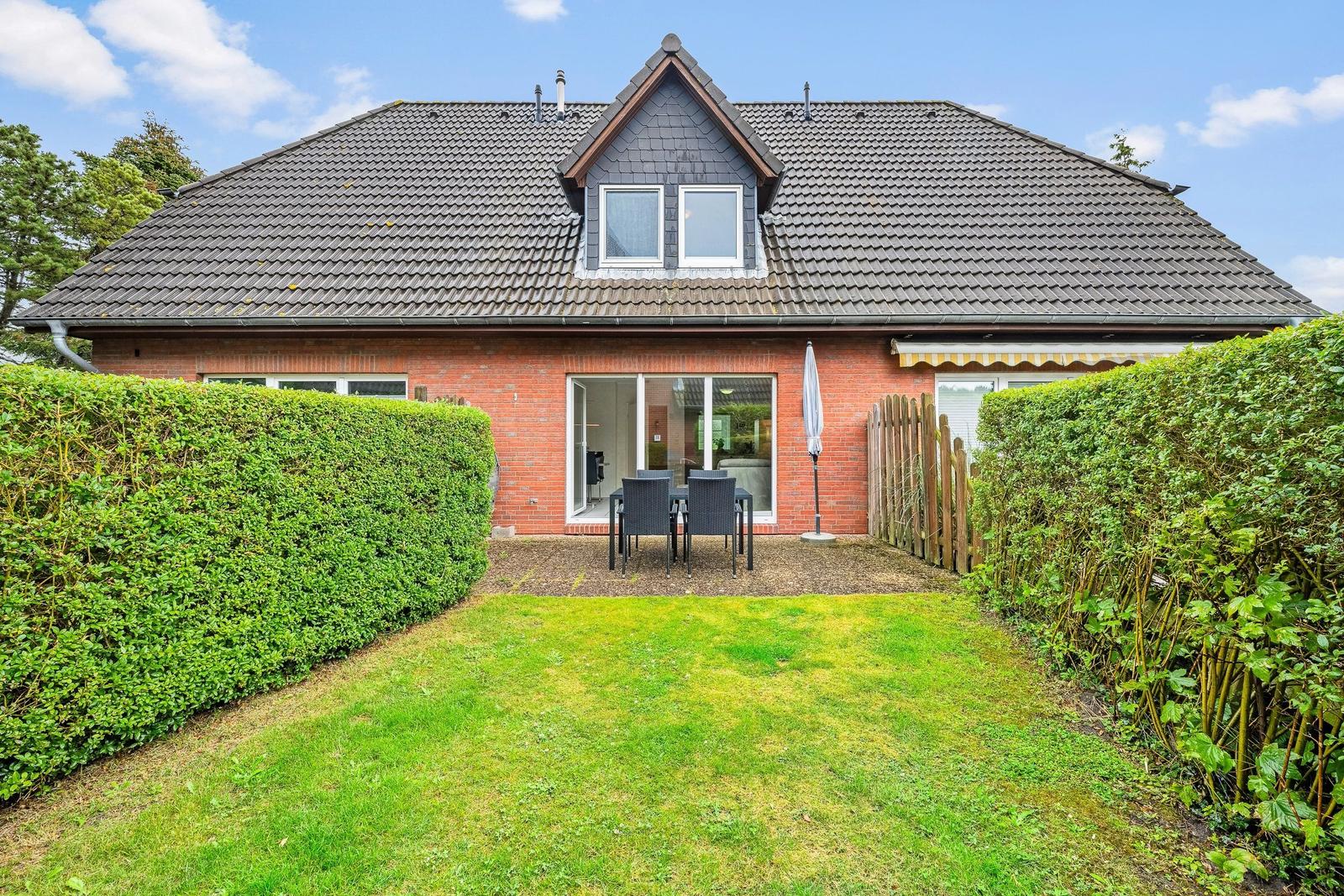 Ein Haus mit rotem Backstein, grauem Dach und Garten mit Tisch und Stühlen.