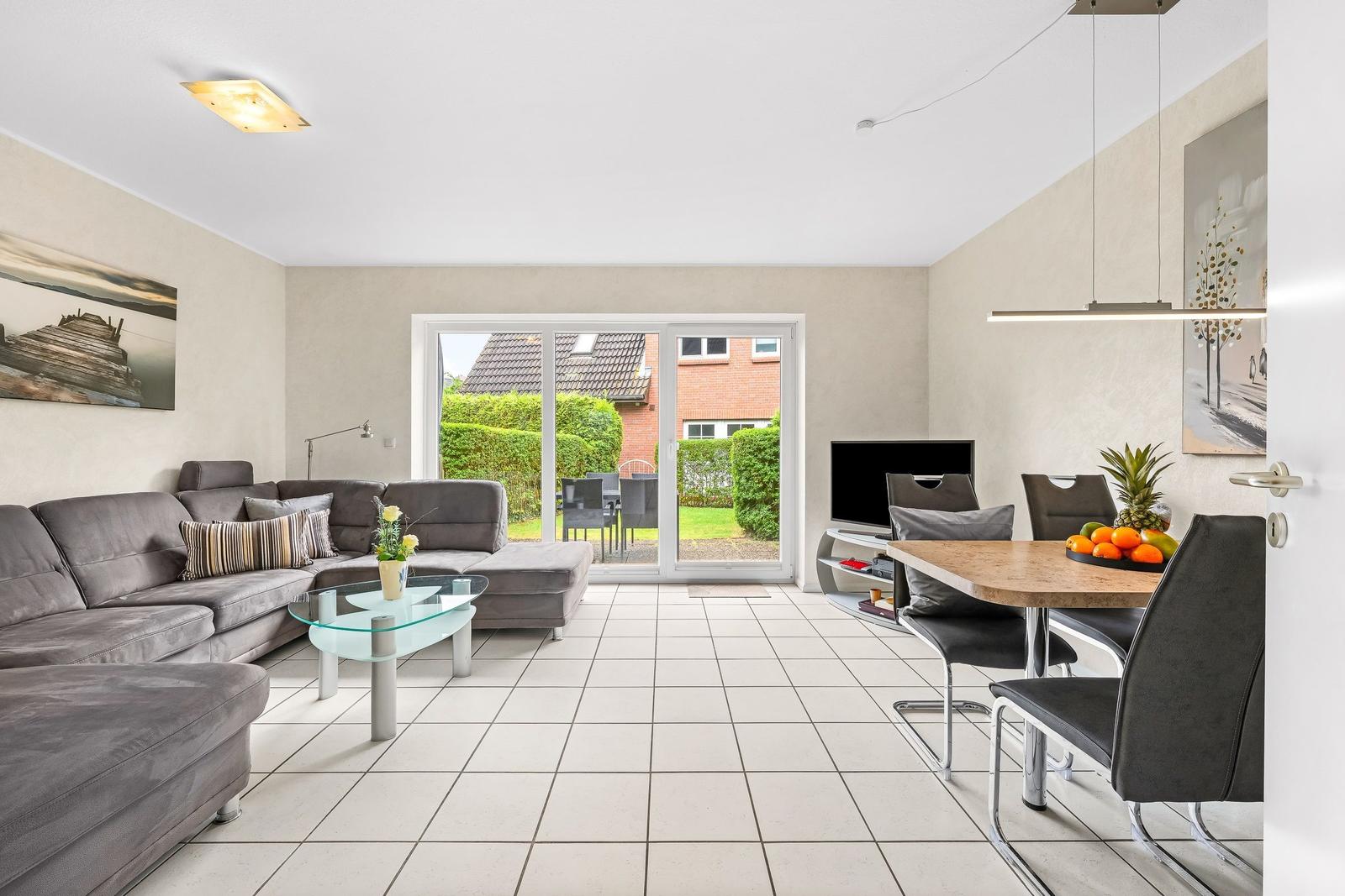 Wohn- und Essbereich mit Sofa, Esstisch und Glastür zum Garten.