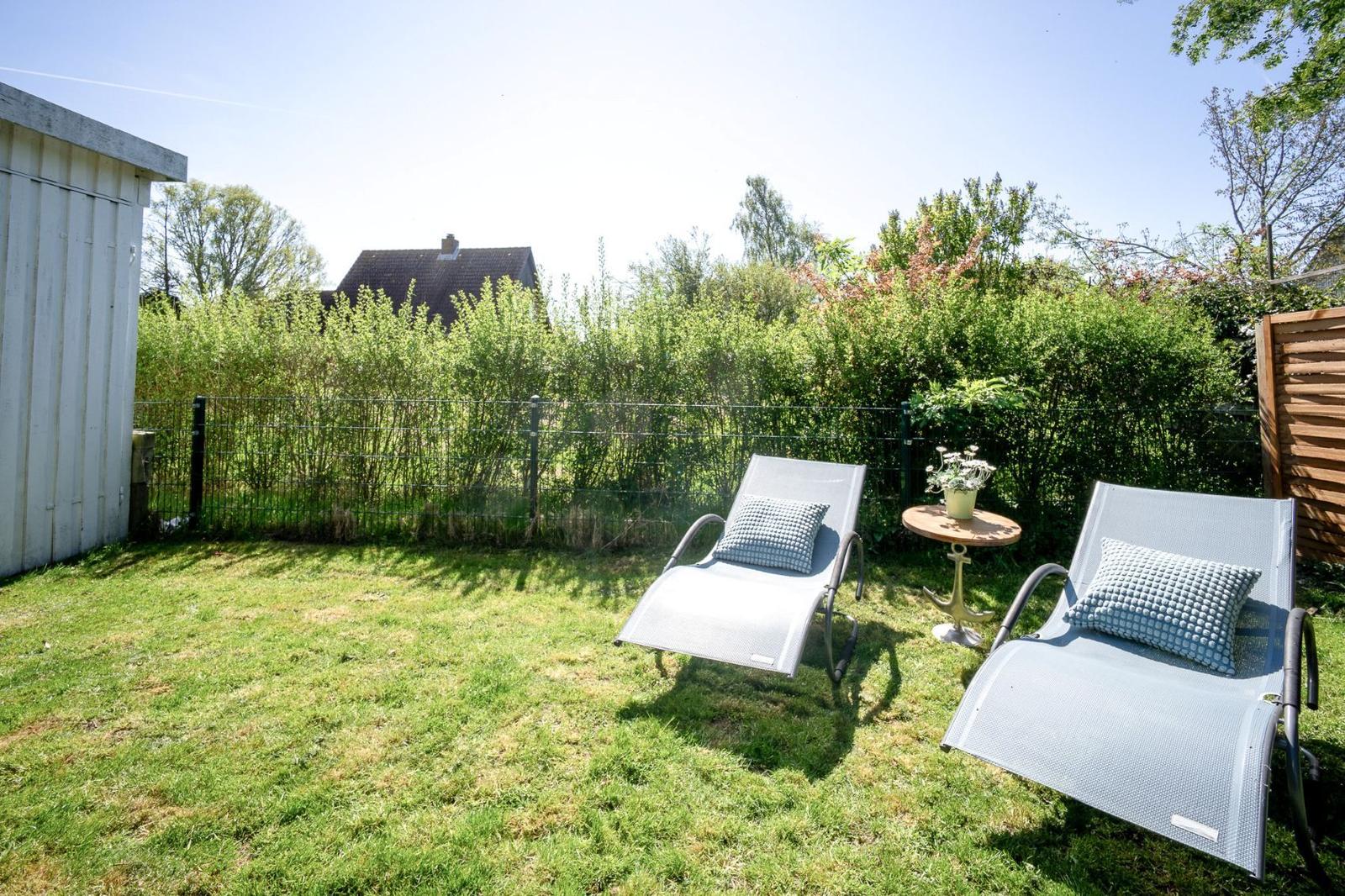 Hinterhof mit zwei Liegestühlen, Tisch und Pflanze. Grasfläche und Hecke im Hintergrund.