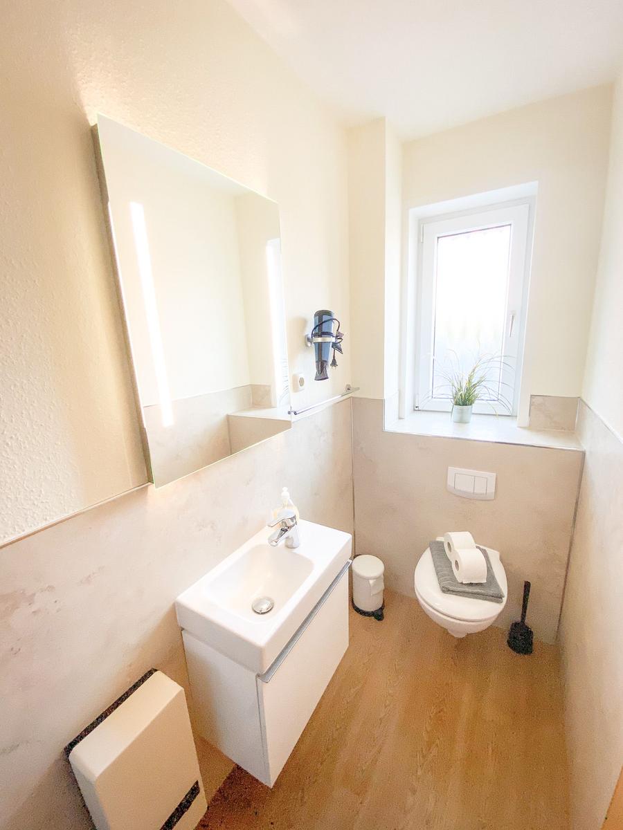 Badezimmer mit Waschbecken, Spiegel, Toilette und Fenster.