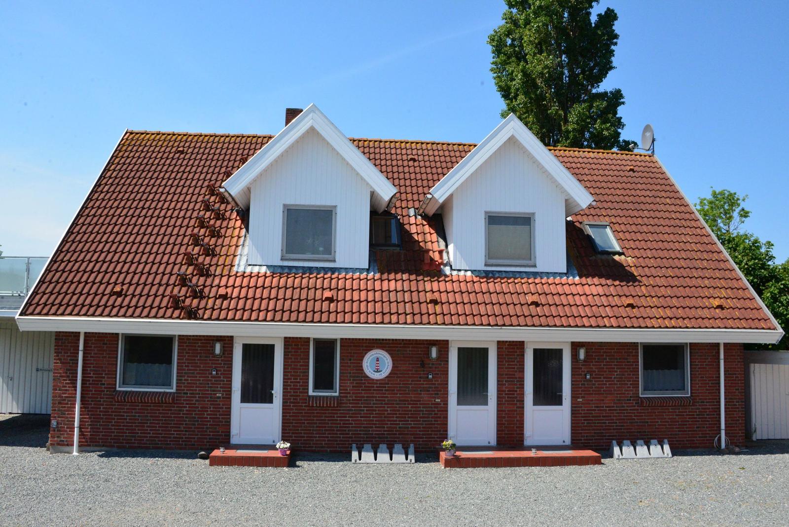 Ferienhaus mit rotem Ziegeldach und weißen Dachgauben. Roter Backsteinbau mit drei Eingängen.