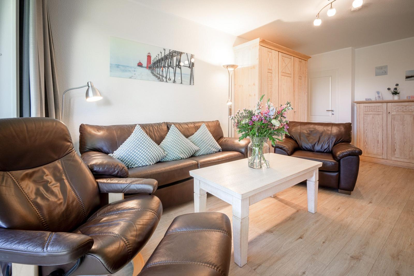 Wohnzimmer mit braunen Ledermöbeln, weißem Tisch und Holzboden.
