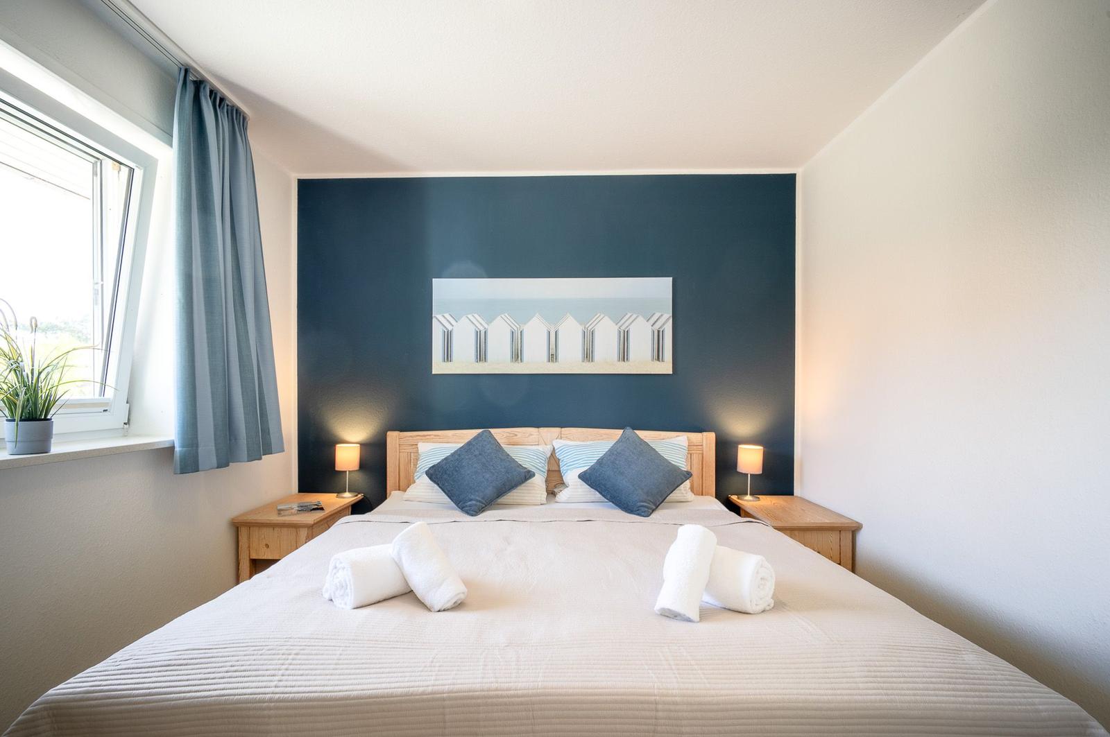 Schlafzimmer mit Bett, Nachttischen und Fenster. Wand mit Kunstwerk.