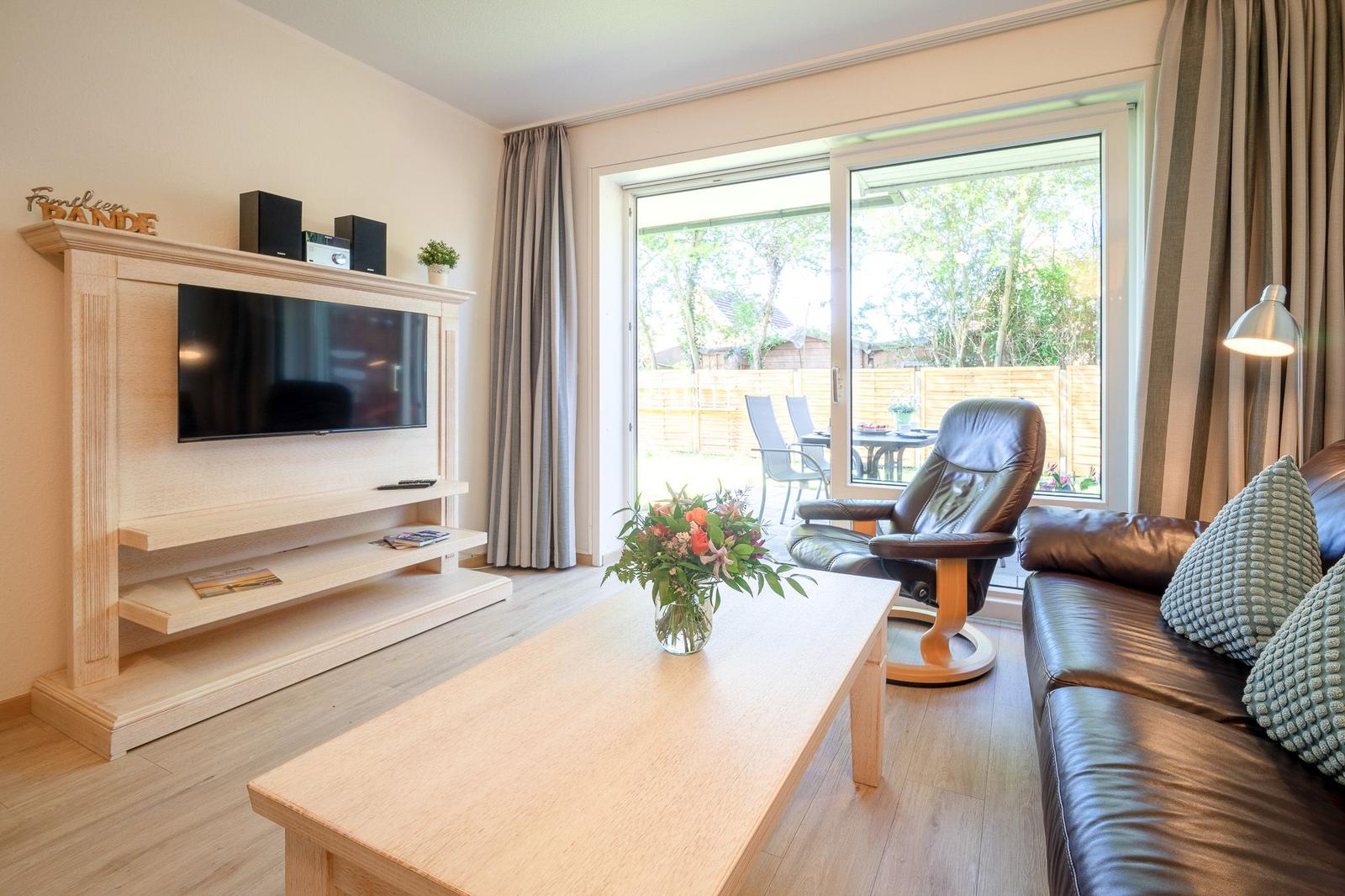 Wohnzimmer mit TV, Sofa, Sessel und Blick auf die Terrasse.