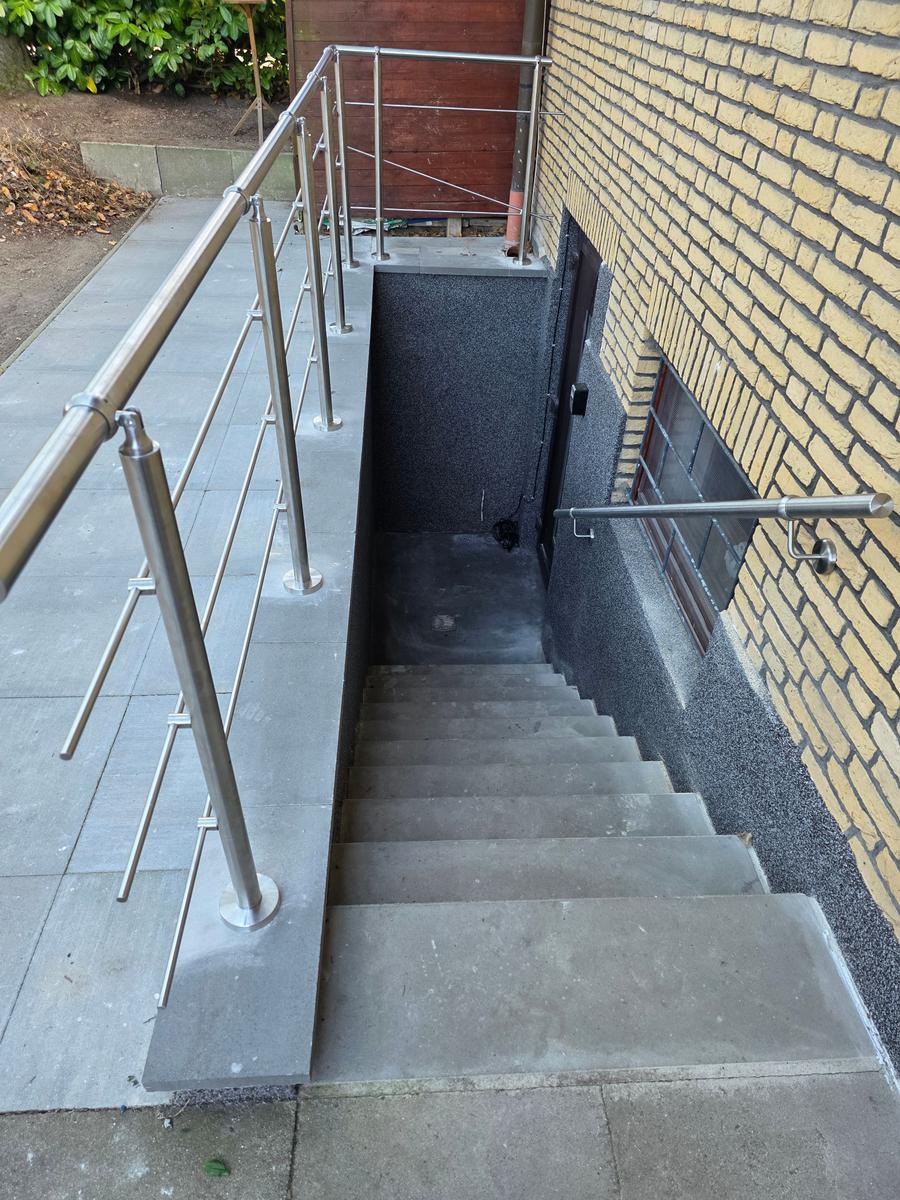 Treppe mit Stahlgeländer führt zu einer Eingangstür im Kellerbereich.