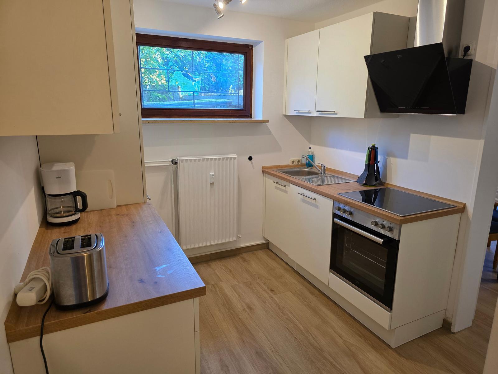 Küche mit Arbeitsplatten, Spüle, Herd und Backofen. Fenster mit Blick auf Garten.