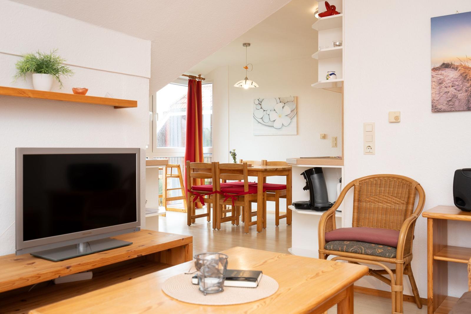 Wohn- und Essbereich mit Fernseher, Esstisch und Stühlen sowie Kaffeemaschine.