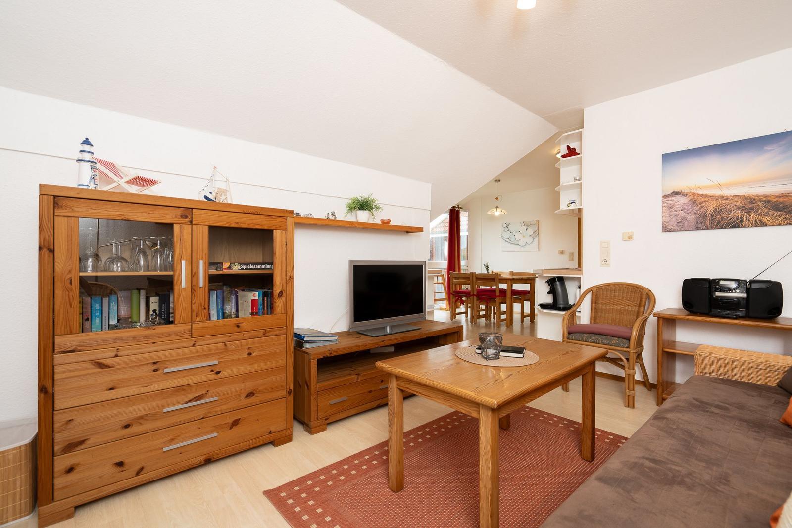 Wohnzimmer mit Holzmöbeln, Fernseher und Essbereich im Hintergrund.