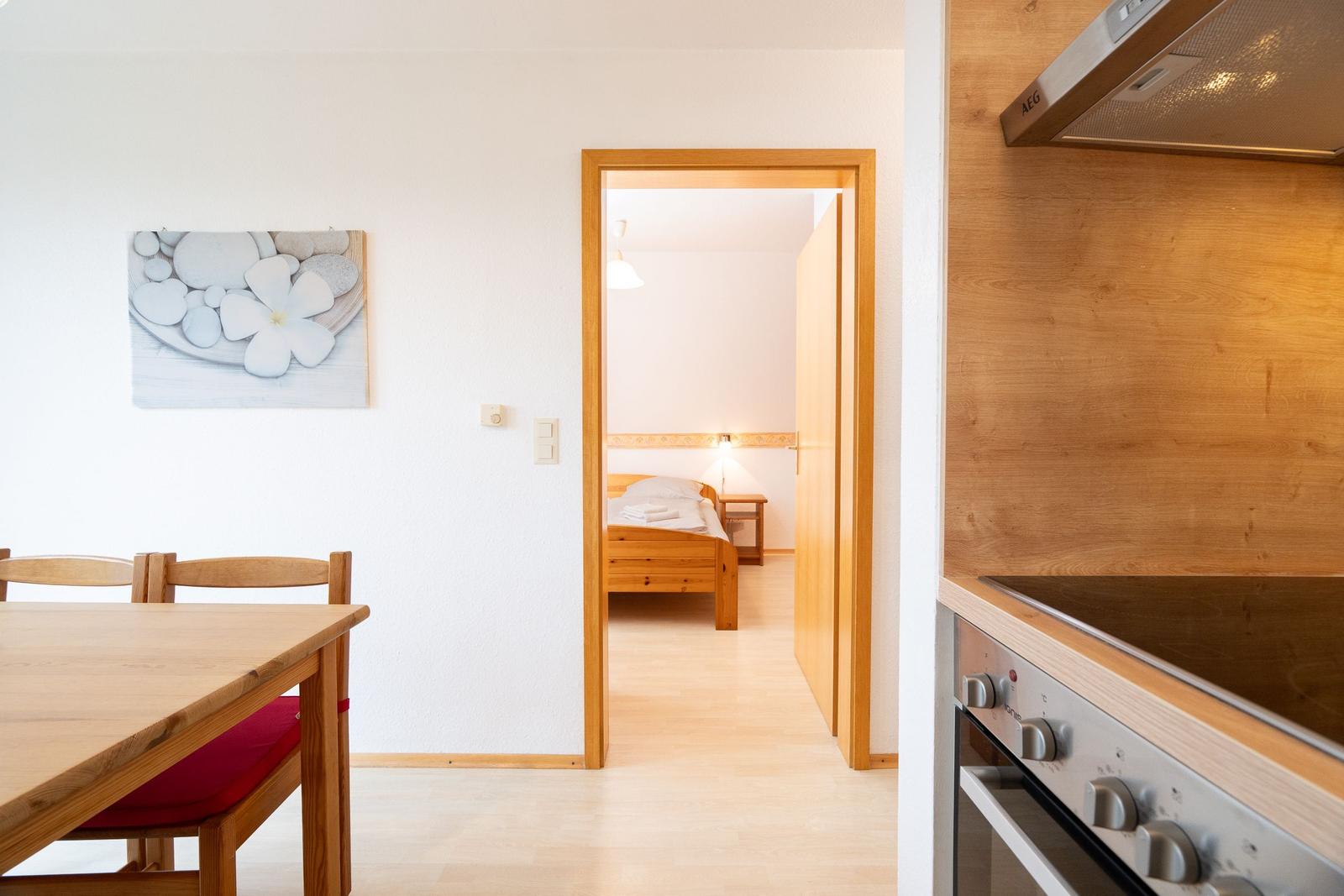 Küche mit Holzoberflächen und Blick in das Schlafzimmer mit Holzbett.