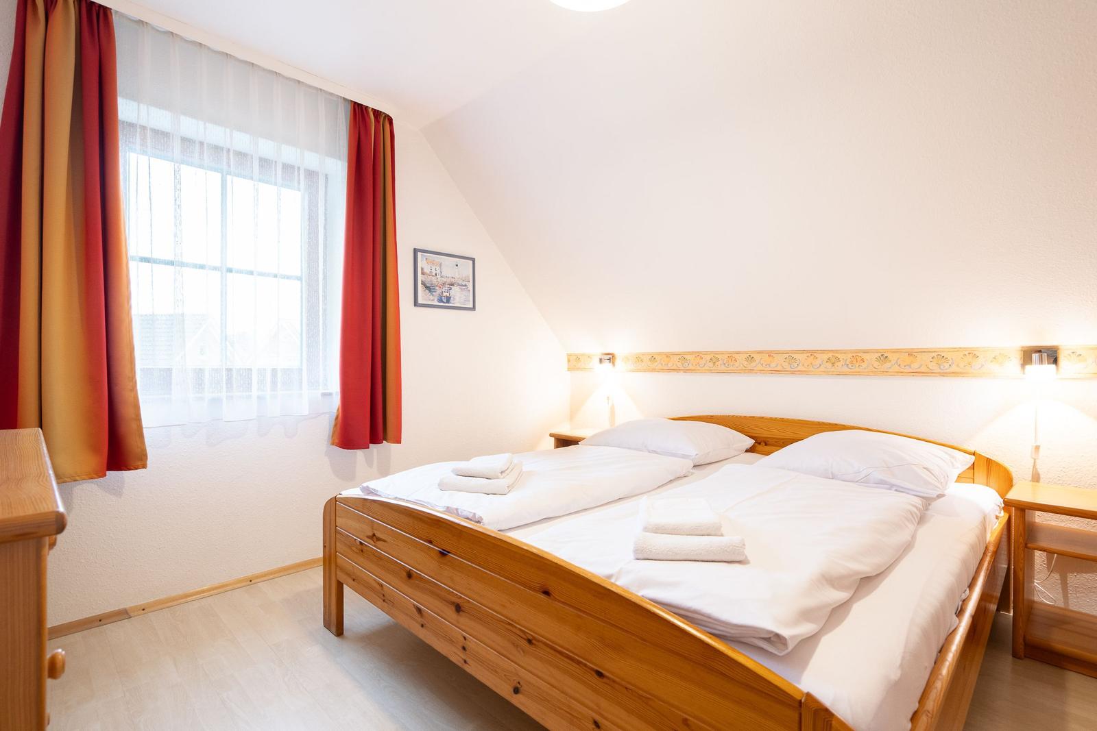 Ein Schlafzimmer mit Holzbett, Fenster und Vorhängen.