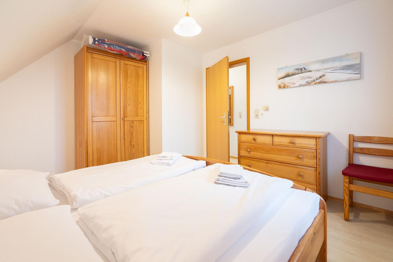 Zimmer mit Doppelbett, Kleiderschrank, Schreibtisch und Stuhl. Decke ist schräg.