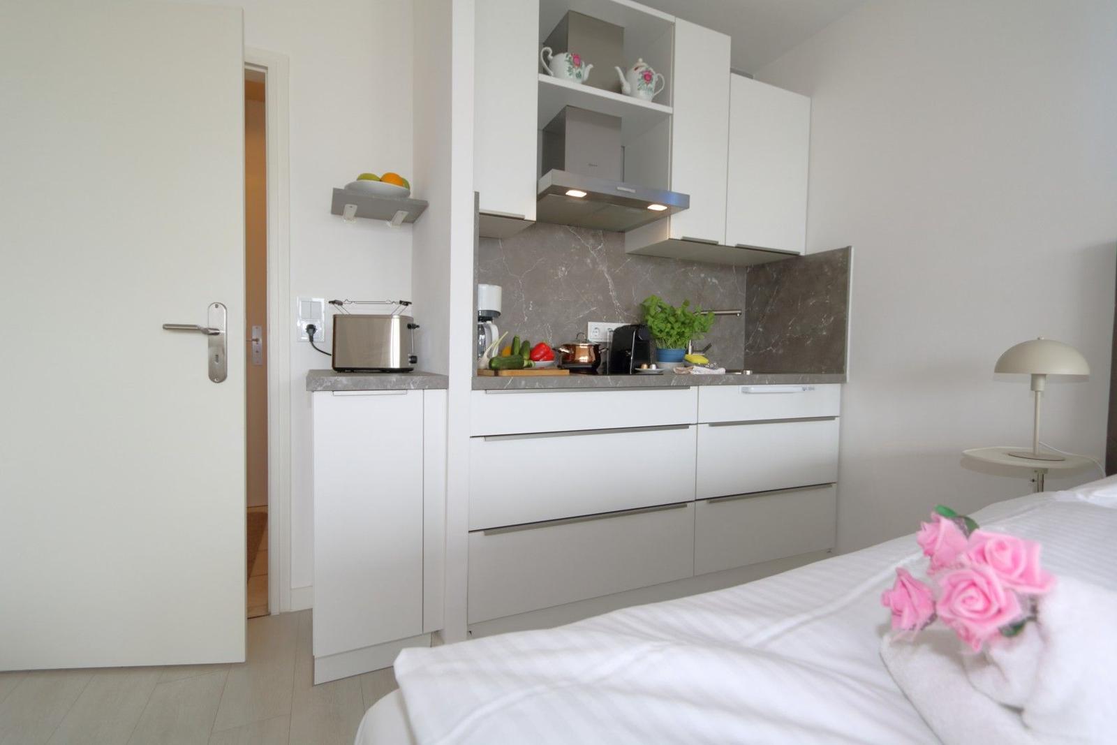 Küche mit Arbeitsplatte, Schränken und Dunstabzug. Bett mit rosa Rosen im Vordergrund.