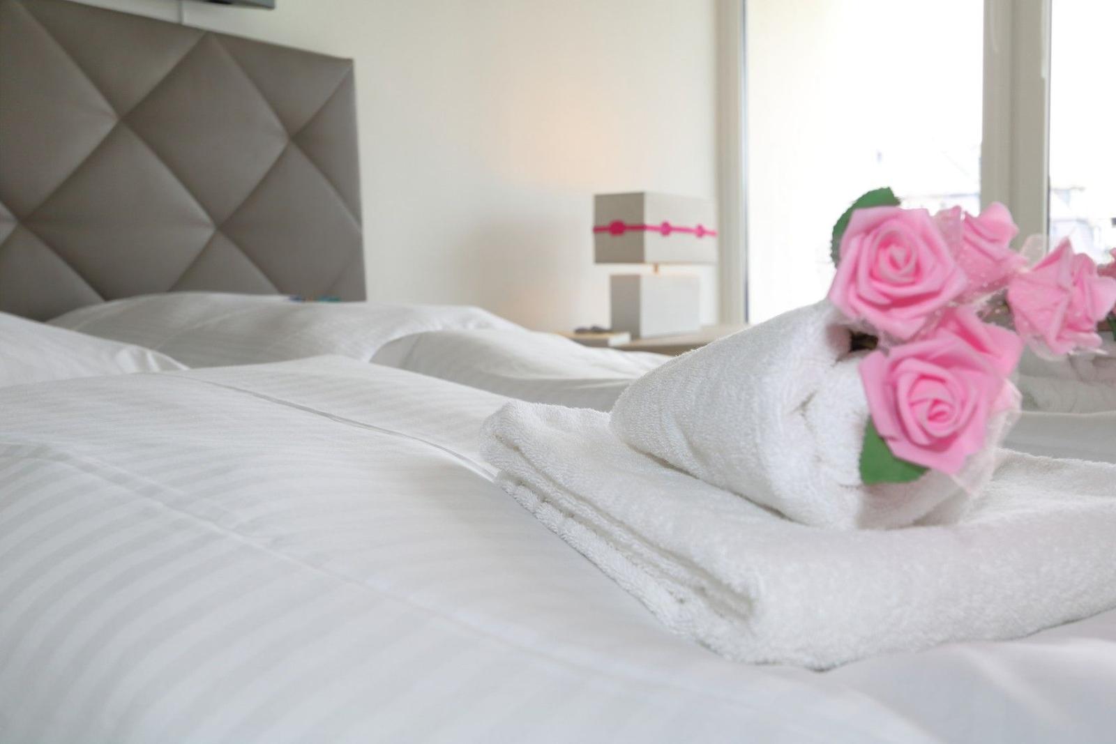 Ein Bett mit weißer Bettwäsche und einem Handtuch, das wie ein Huhn mit rosa Rosen aussieht.