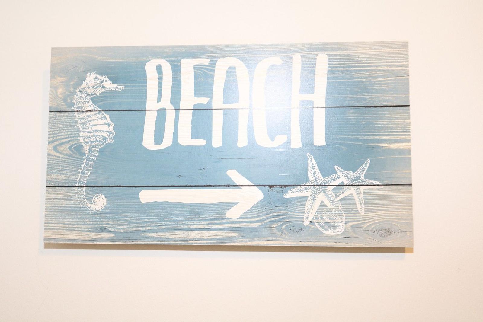 Holzschild mit BEACH und Pfeil zeigt Richtung Strand. Zeichnungen von Seepferdchen und Sternenfischen.