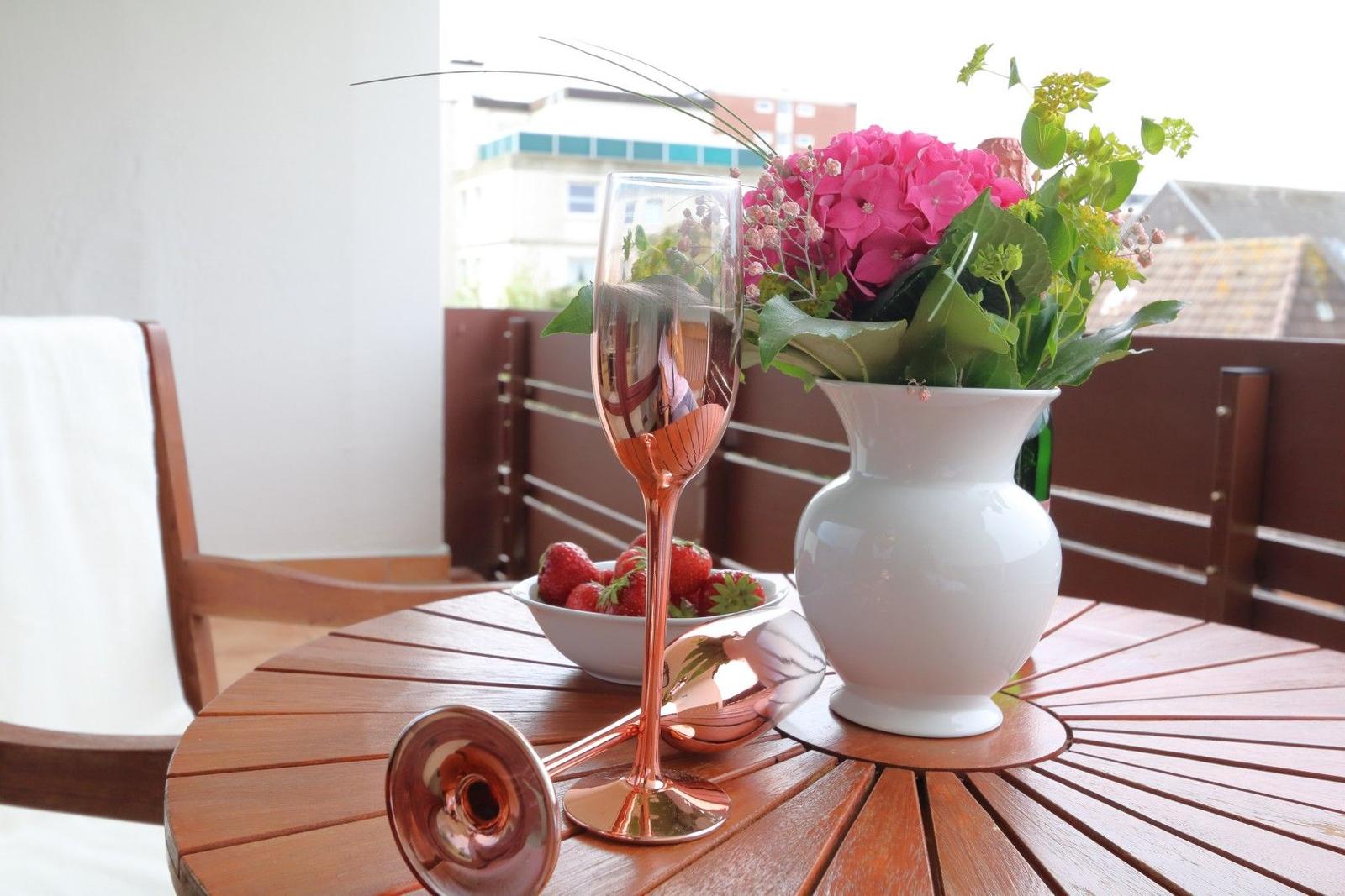 Auf der Terrasse steht ein Tisch mit Blumen, Wein und Erdbeeren.