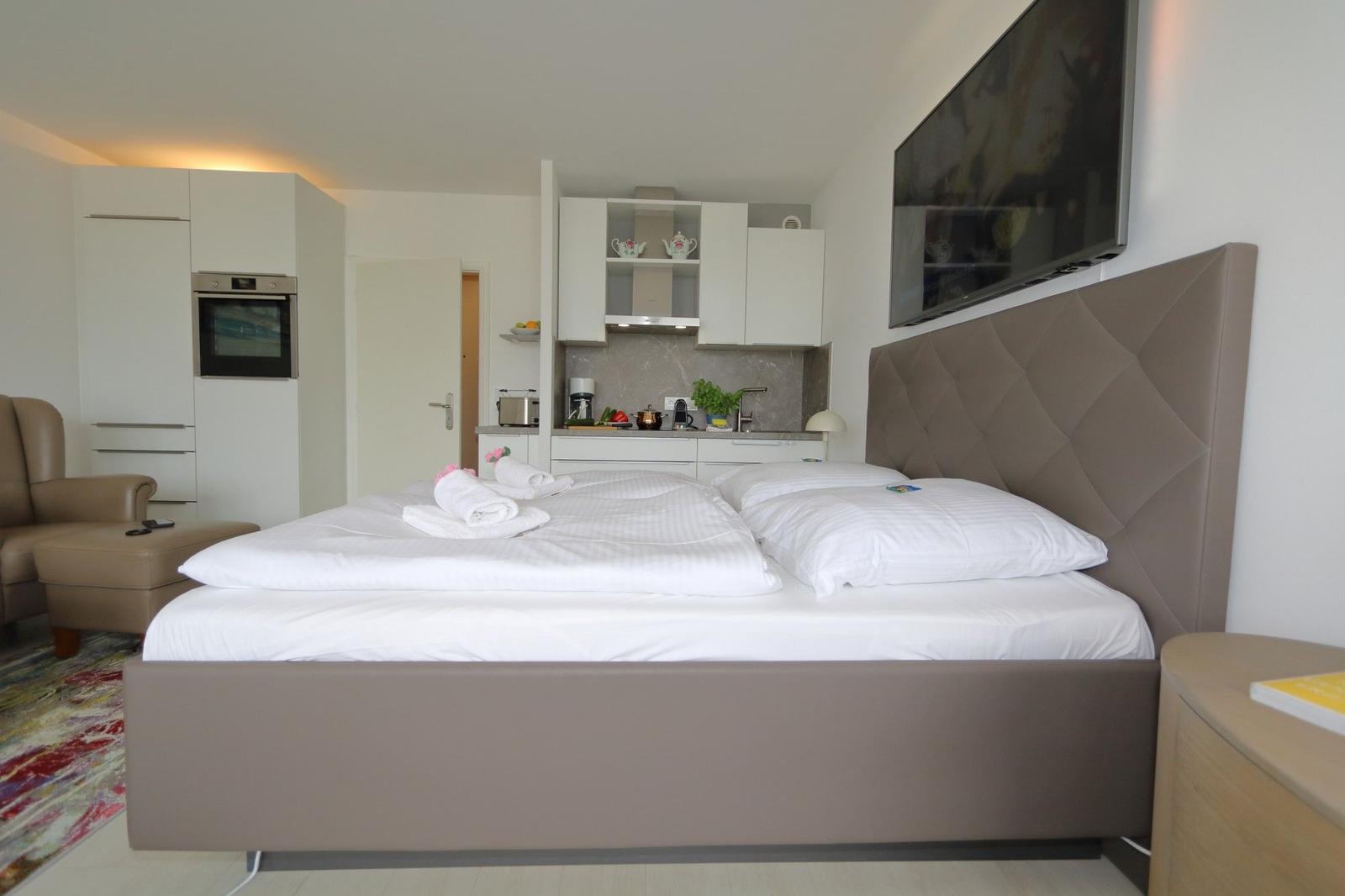 Schlafzimmer mit Doppelbett, Küchenzeile und Fernseher an der Wand.