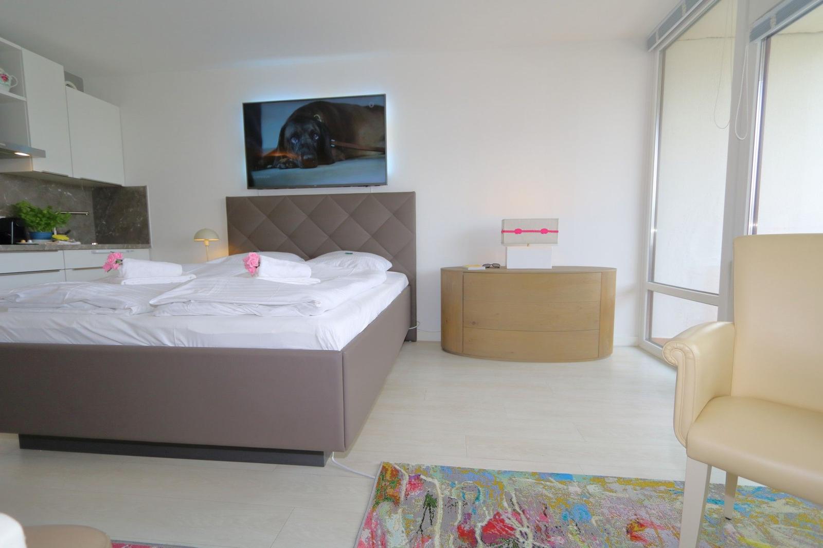 Schlafzimmer mit Doppelbett, Fernseher und integrierter Küche.