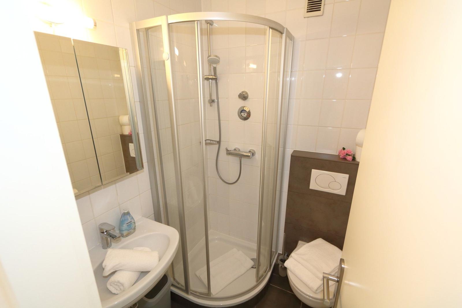 Badezimmer mit Dusche, Waschbecken und Toilette. Weiße Fliesen und Handtücher.
