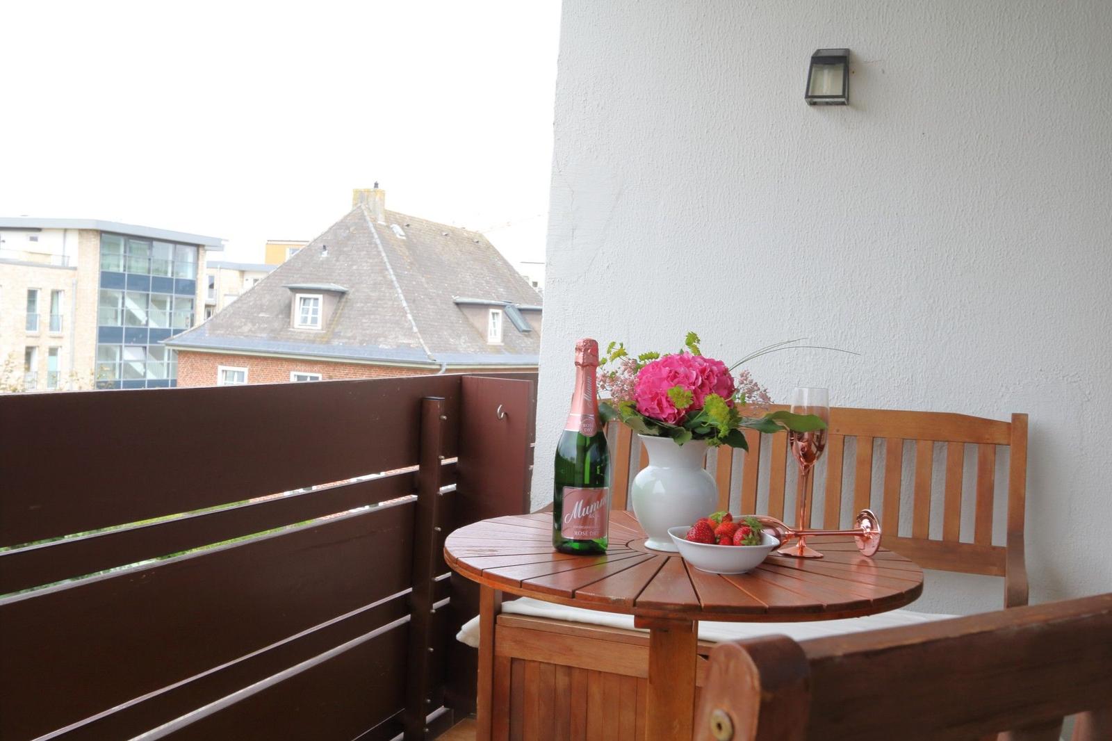 Terrasse mit Tisch, Stühlen, Blumen und einer Flasche Sekt.