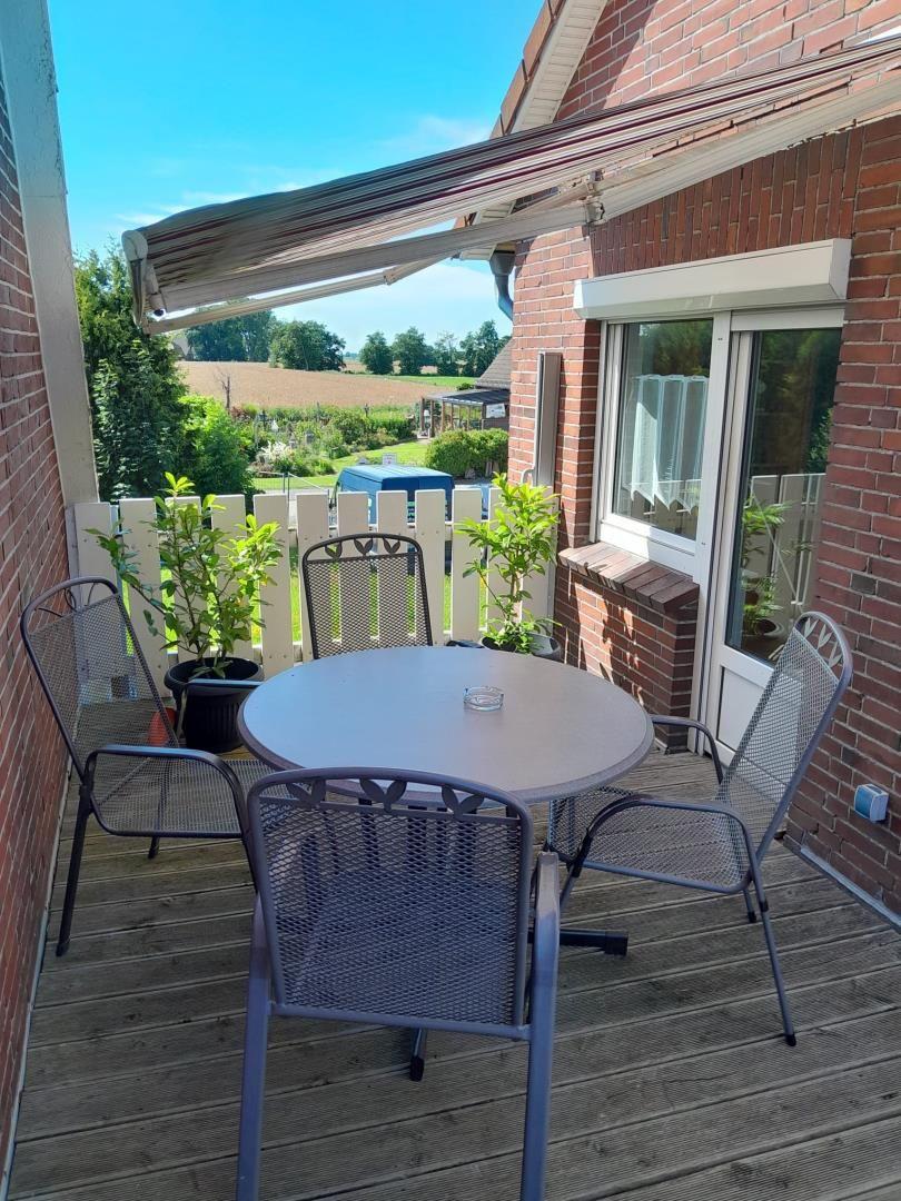 Terrasse mit Tisch und Stühlen, Sonnenschutz, Blick auf Garten und Feld.