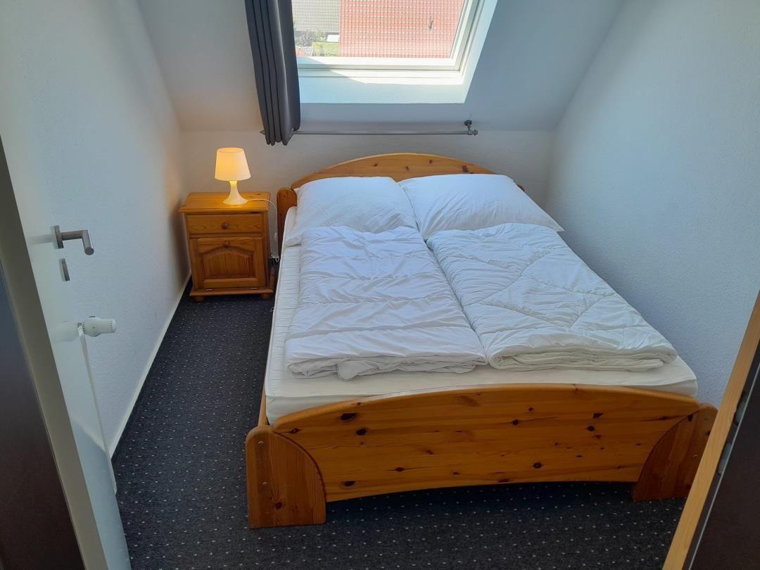 Schlafzimmer mit Holzbett, Nachttisch und Dachfenster.