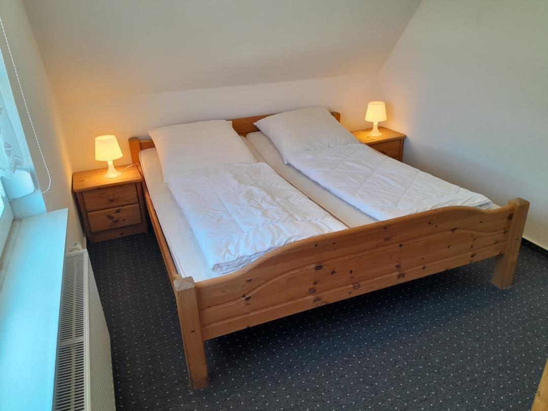 Schlafzimmer mit Doppelbett, zwei Nachttischen und Lampen. Dachgeschoss mit Fenster und Heizung.
