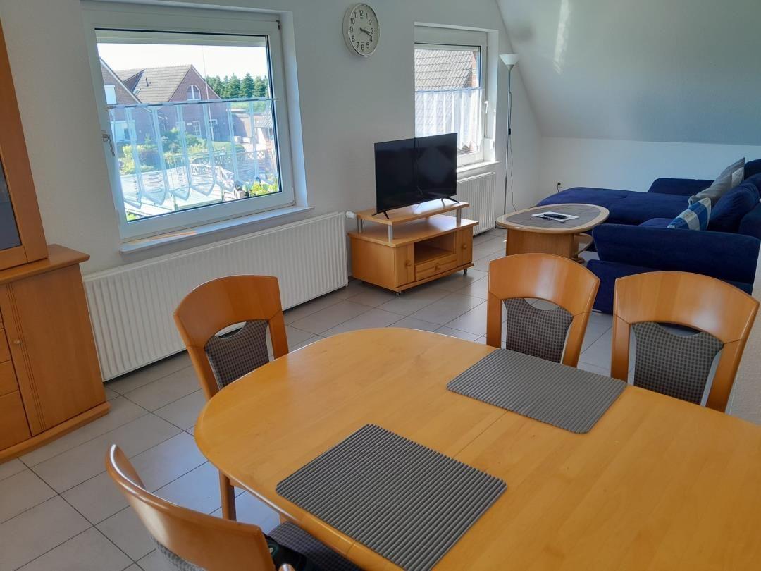 Esszimmer mit Holztisch und Stühlen, Wohnbereich mit Sofa und Fernseher.