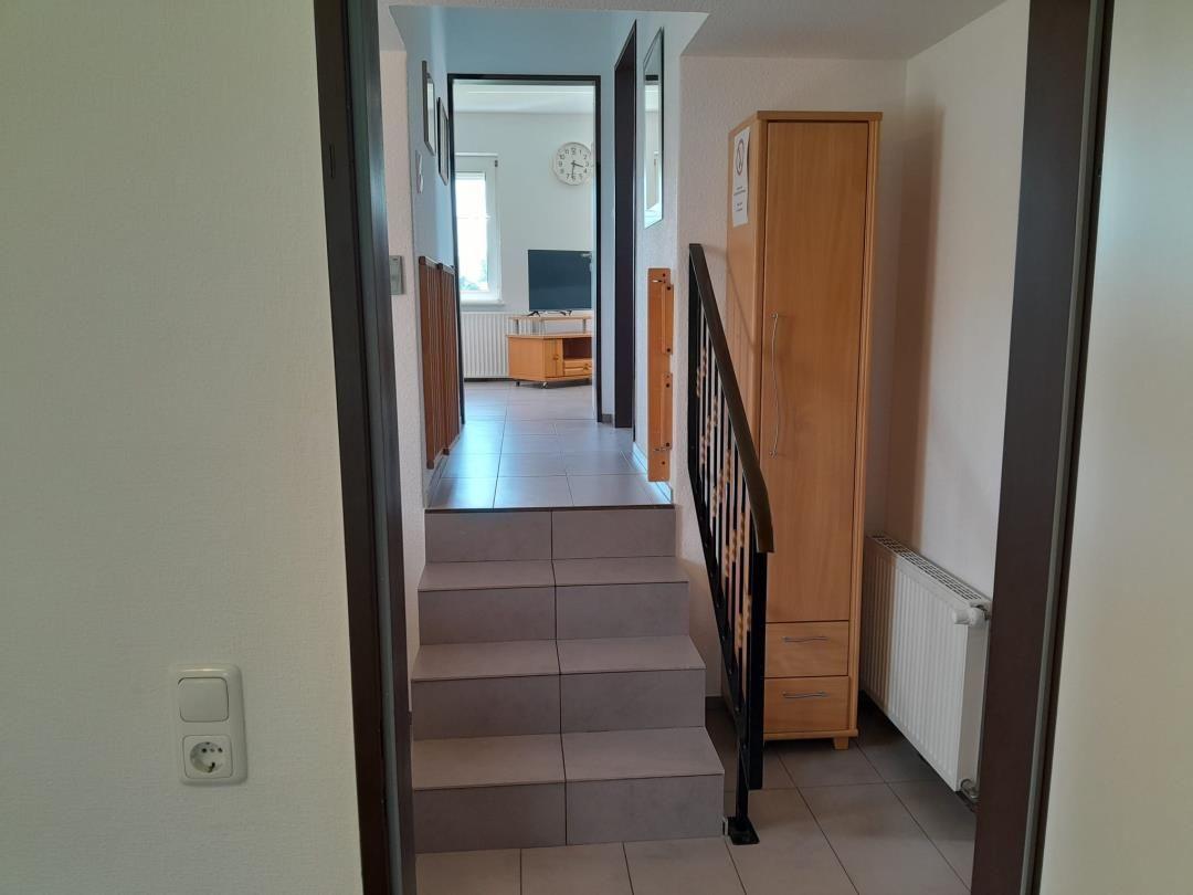 Hausflur mit Treppe, Kleiderschrank und Blick in Wohnzimmer.