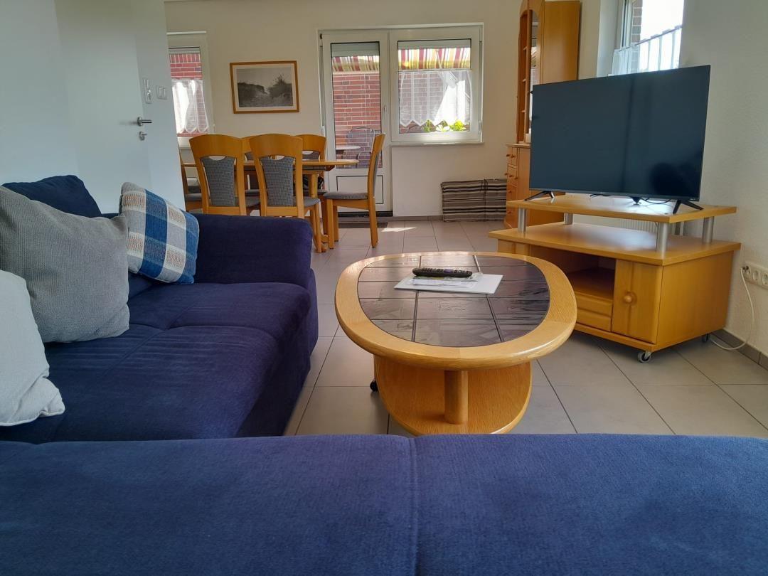 Wohnzimmer mit Sofa, Couchtisch und Fernseher. Im Hintergrund ist das Esszimmer zu sehen.